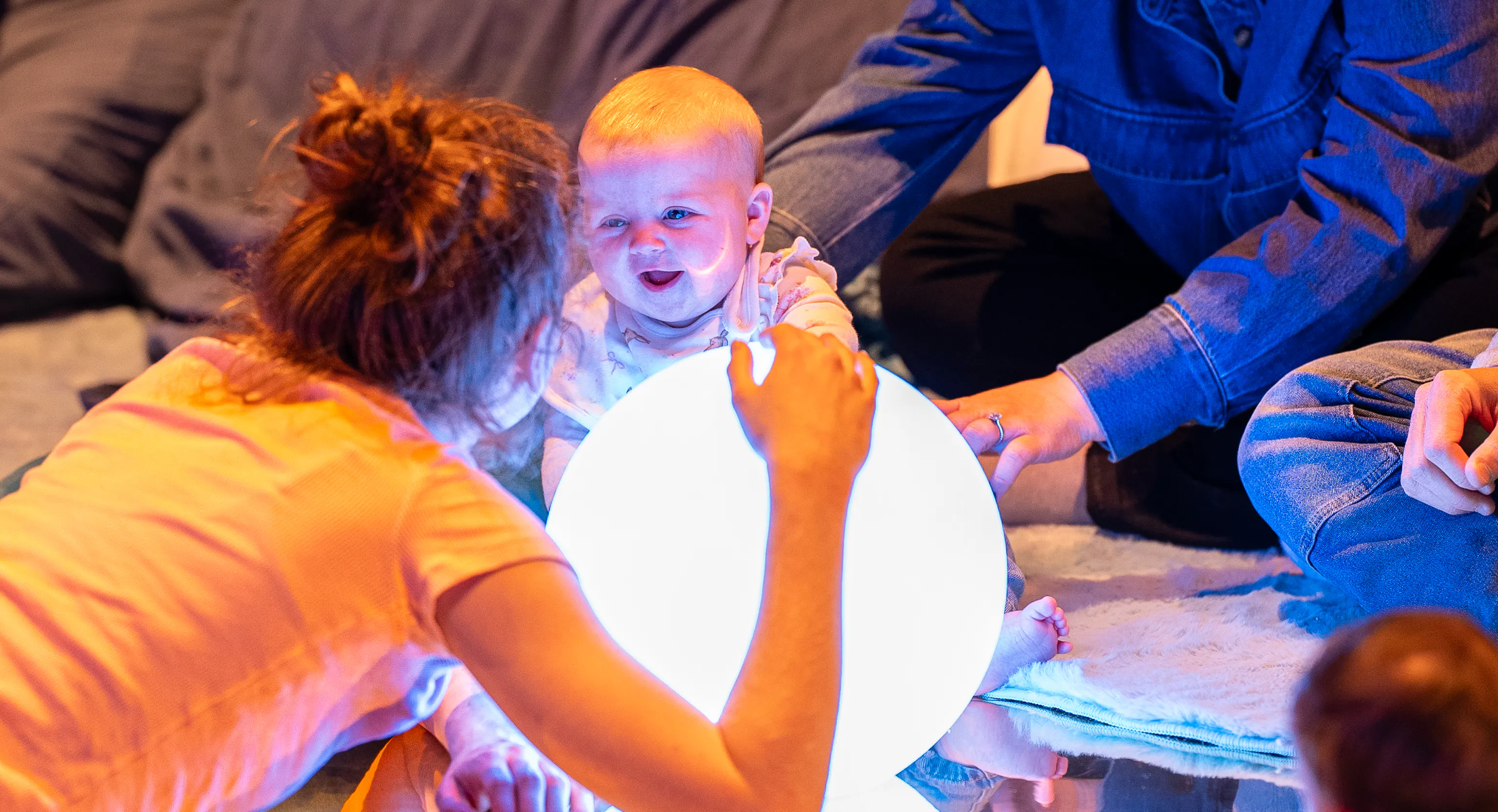 Parent / carer and baby engaging with big spherical light. Both are smiling.