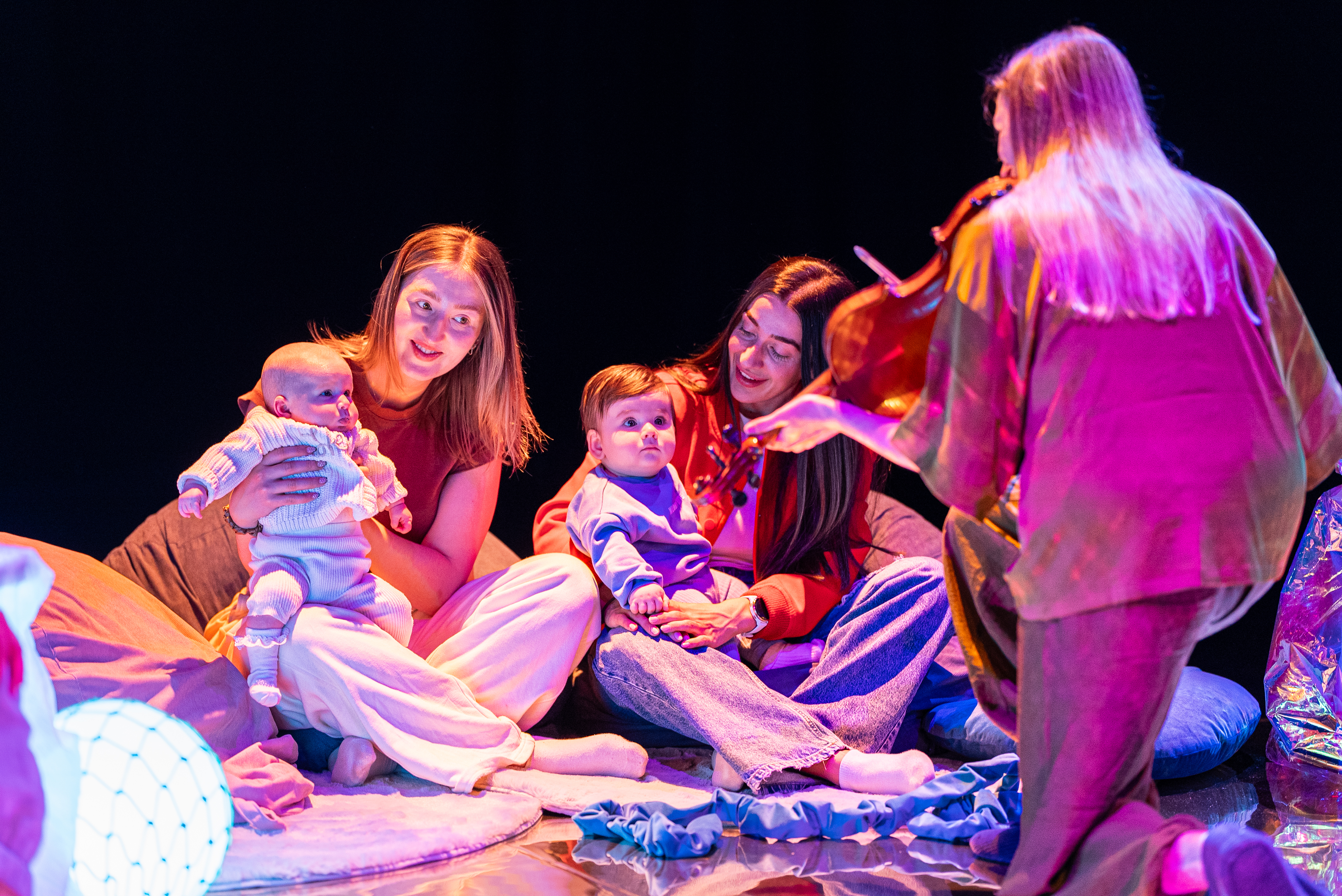 a group of parents/carers and their babies engage with a performer playing violin.