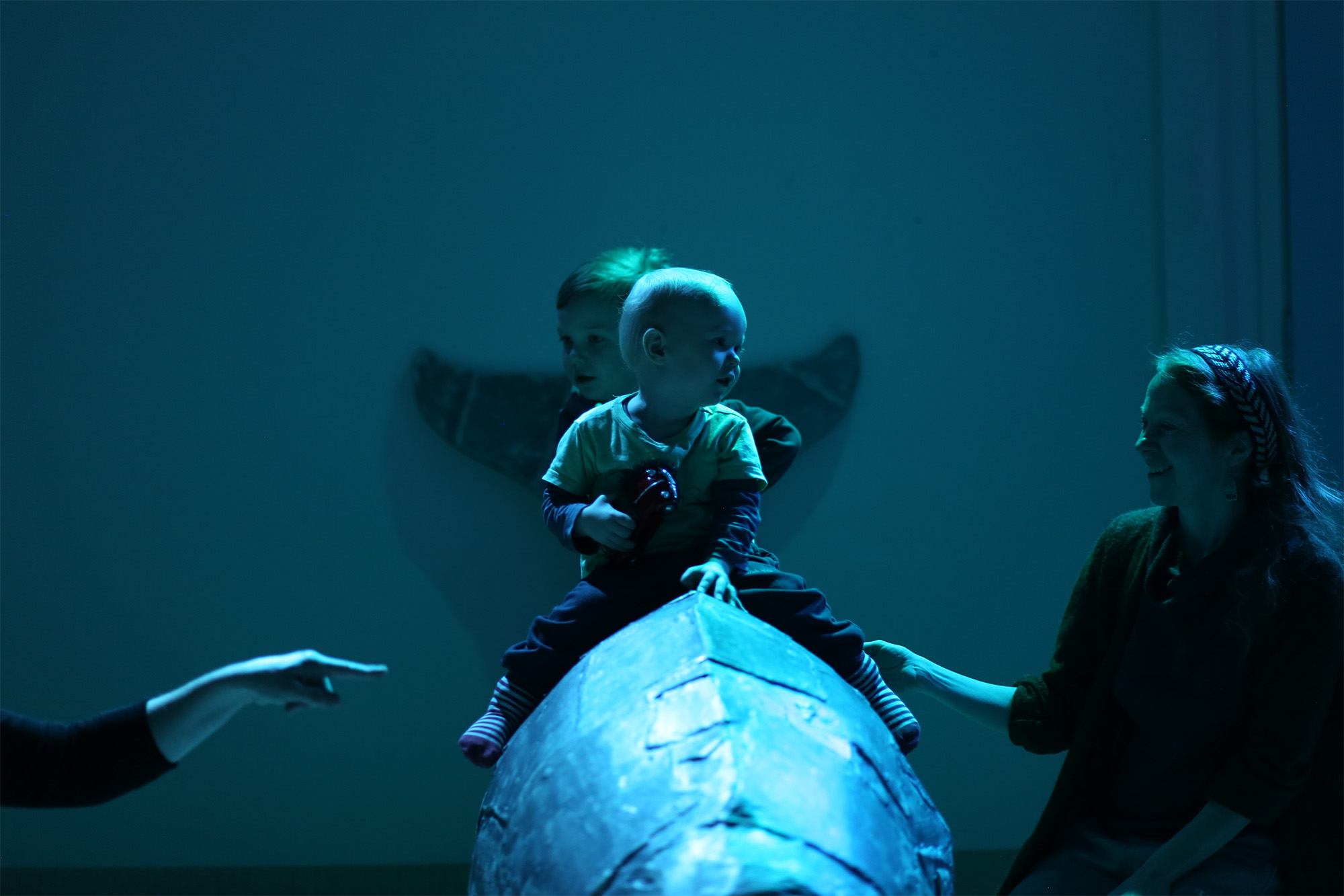 Two babies sat on an object in a darkly lit blue room