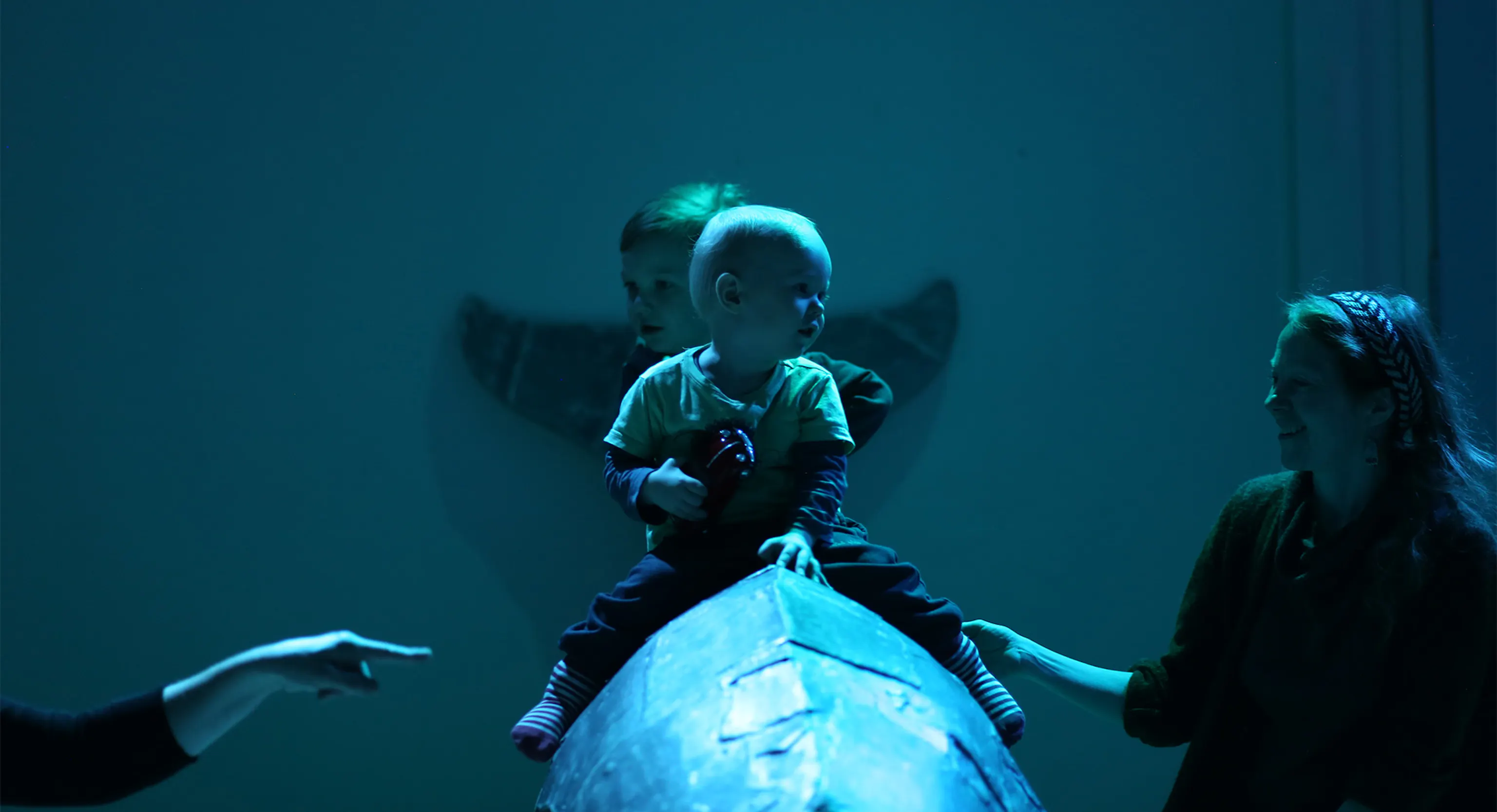 Two babies sat on an object in a darkly lit blue room