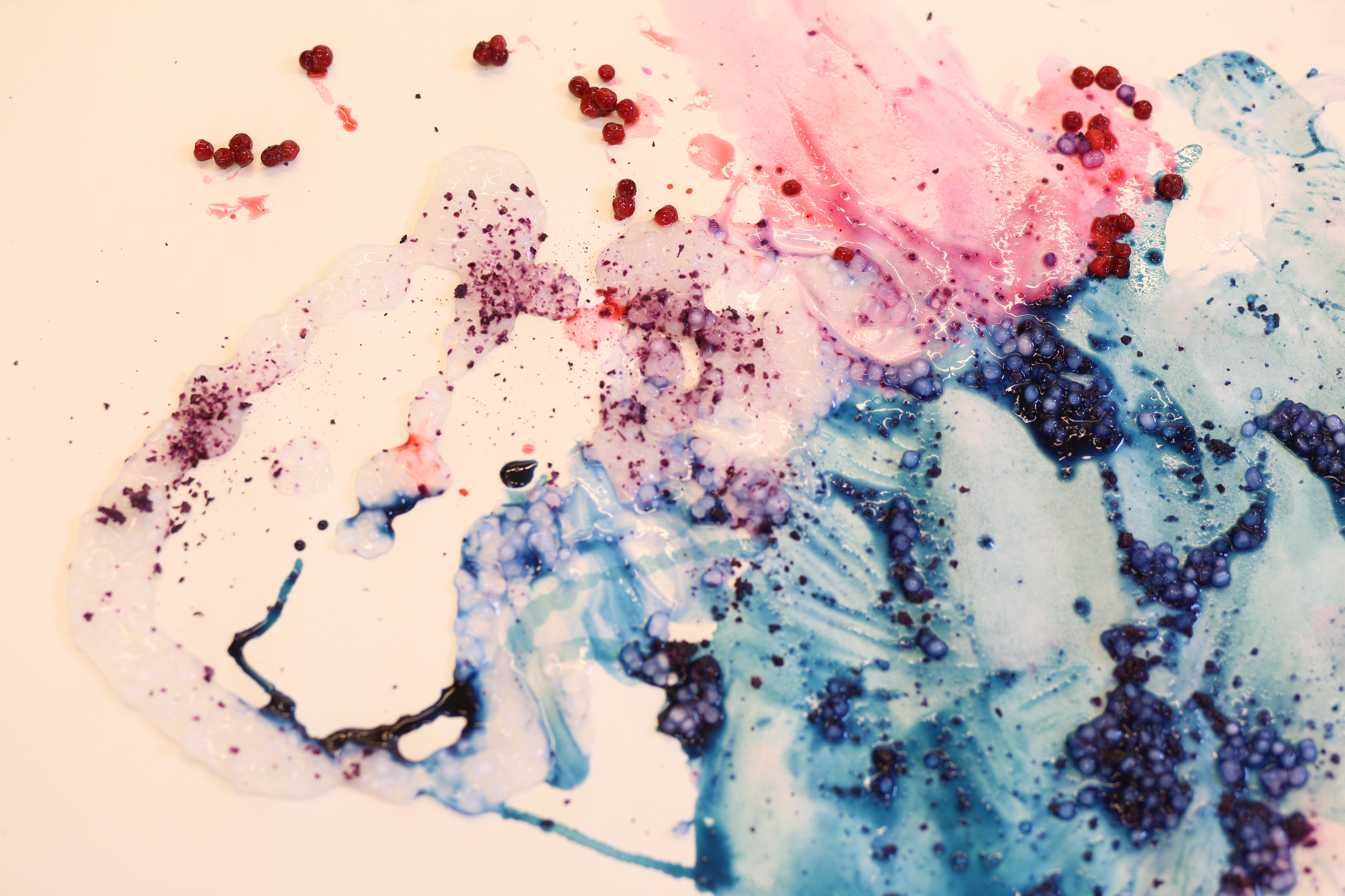 A colourful piece of paper that resembles a painting. There is fruit on the paper which has created the blue and red colours