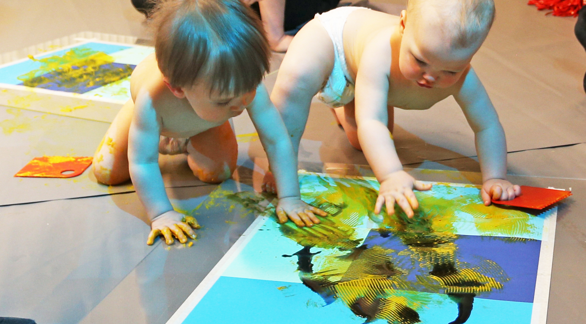 Two babies touching a piece of paper with yellow material 