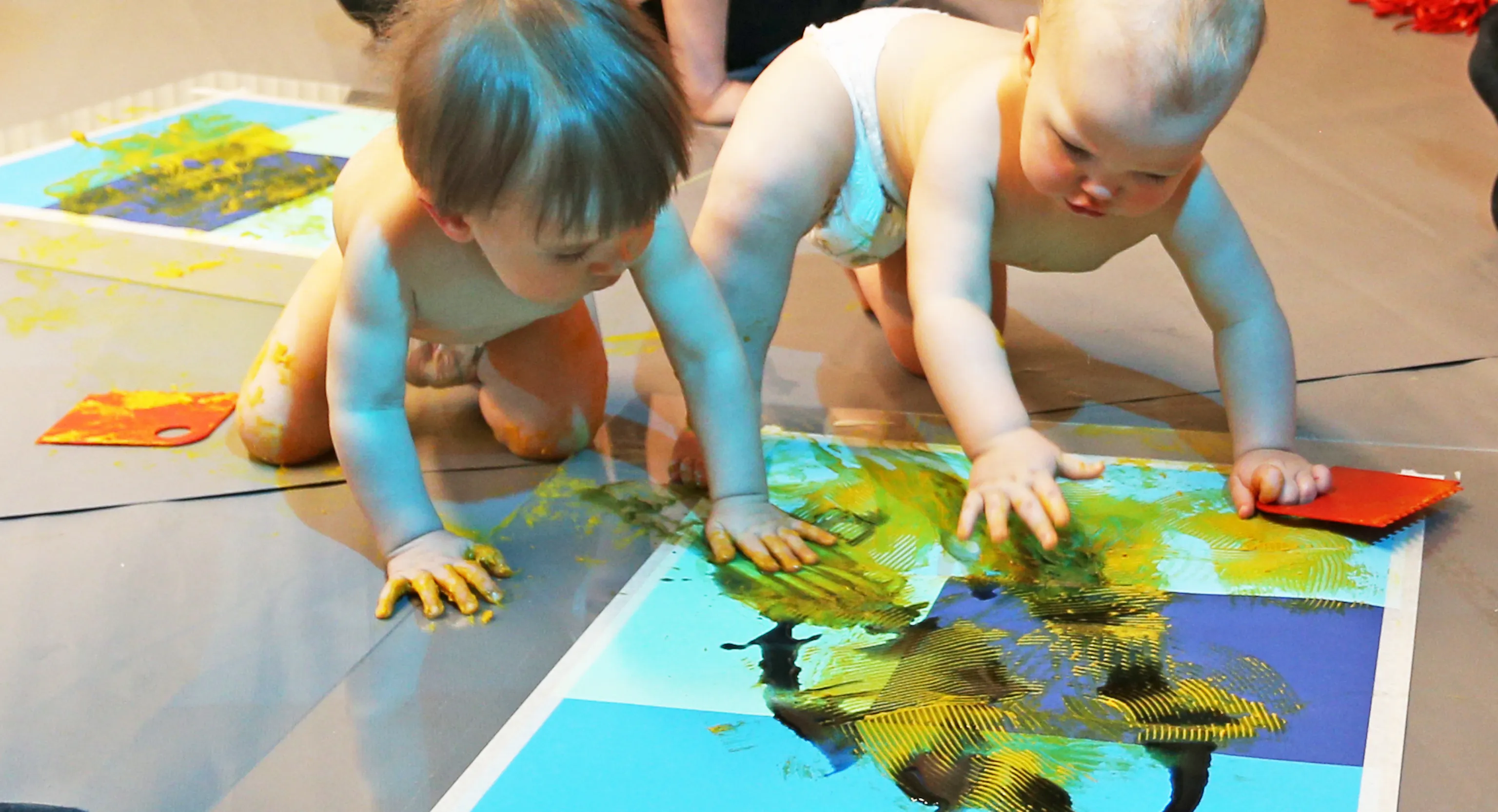 Two babies touching a piece of paper with yellow material