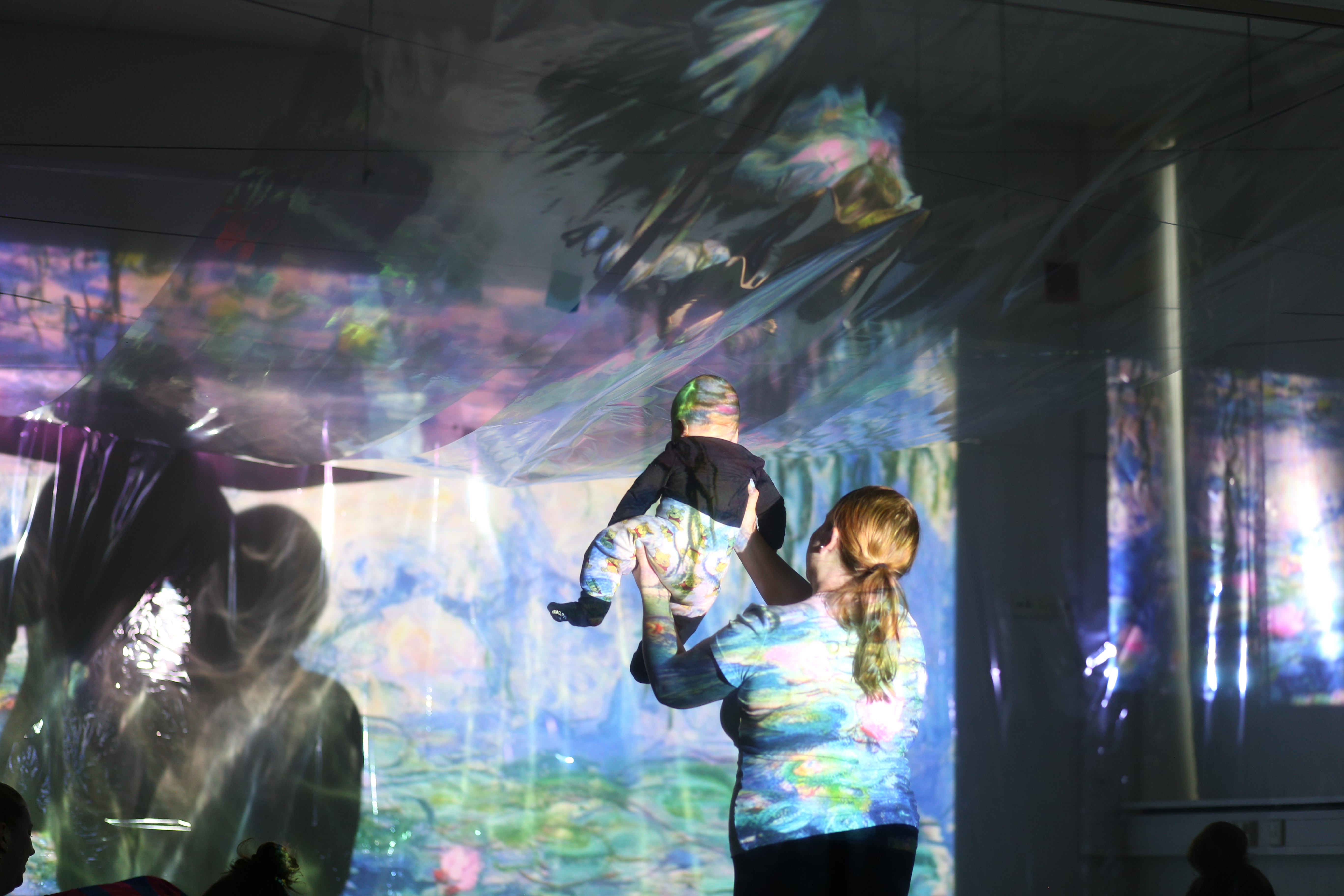 A parent holds up a baby in front of colour projections 