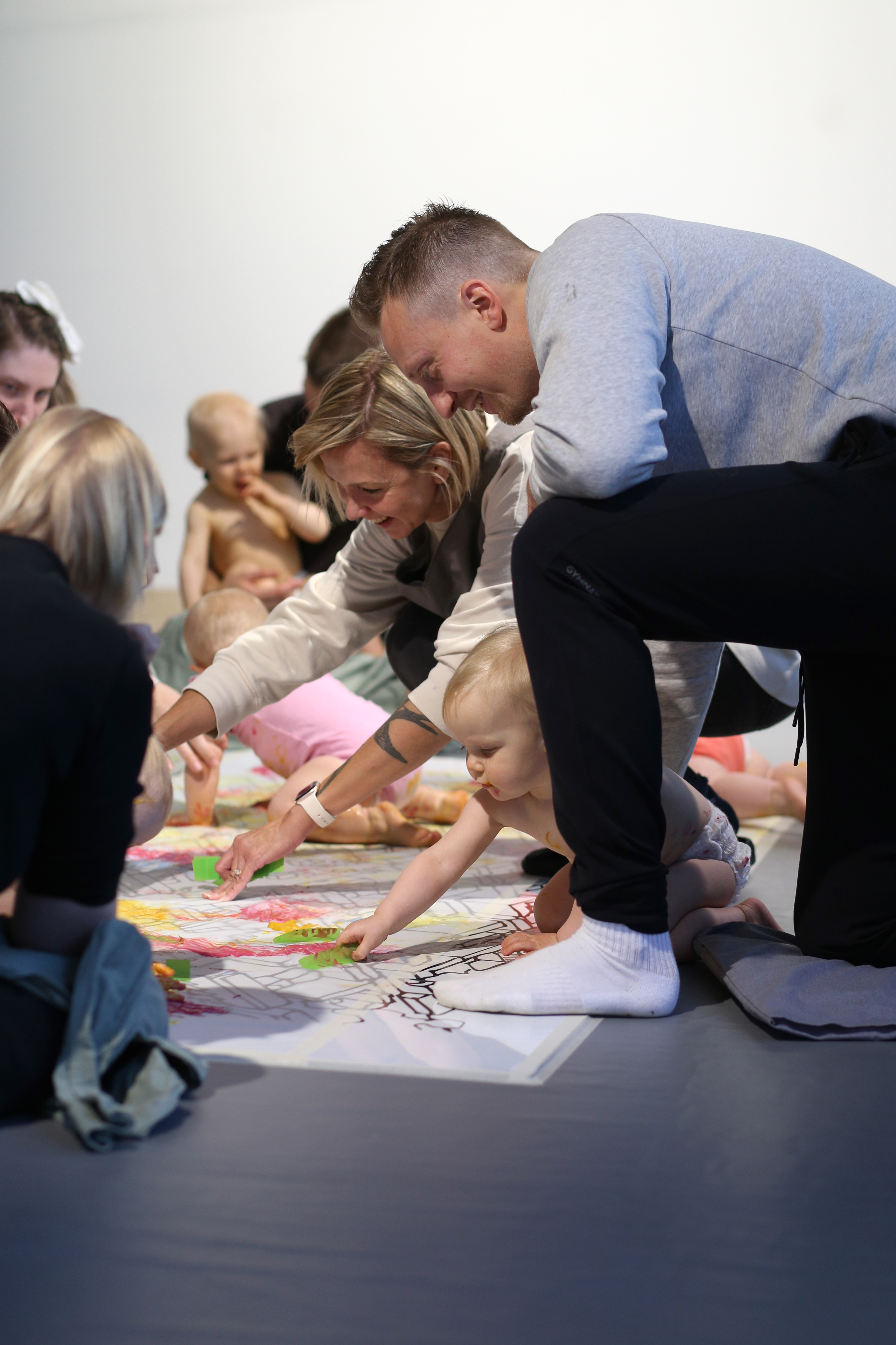 A group of babies with their parents and carers engaging in a colour workshop - touching paper on the floor with colourful hands 