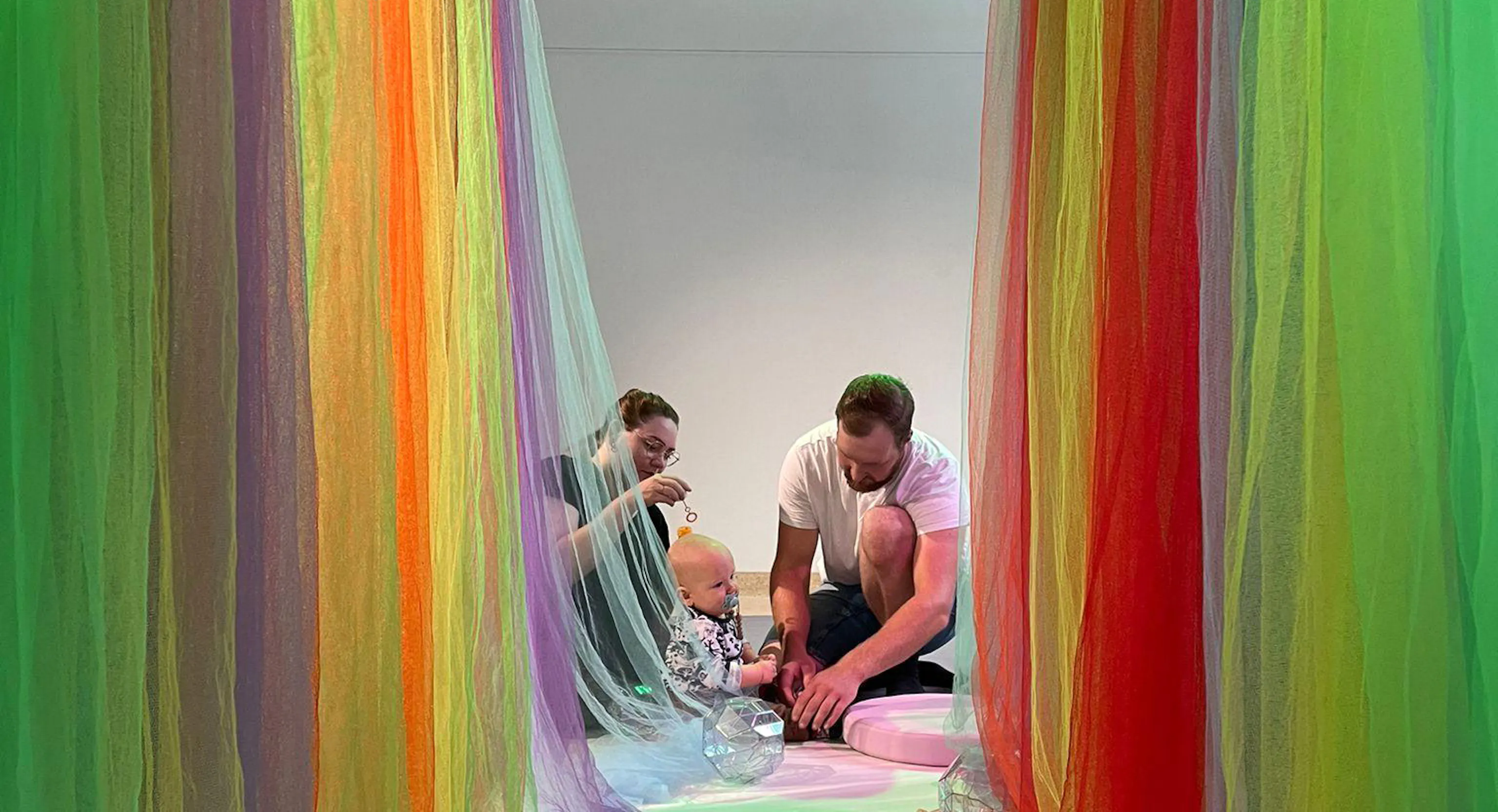 A baby and their parents and carers at the end of a hall filled with colourful materials