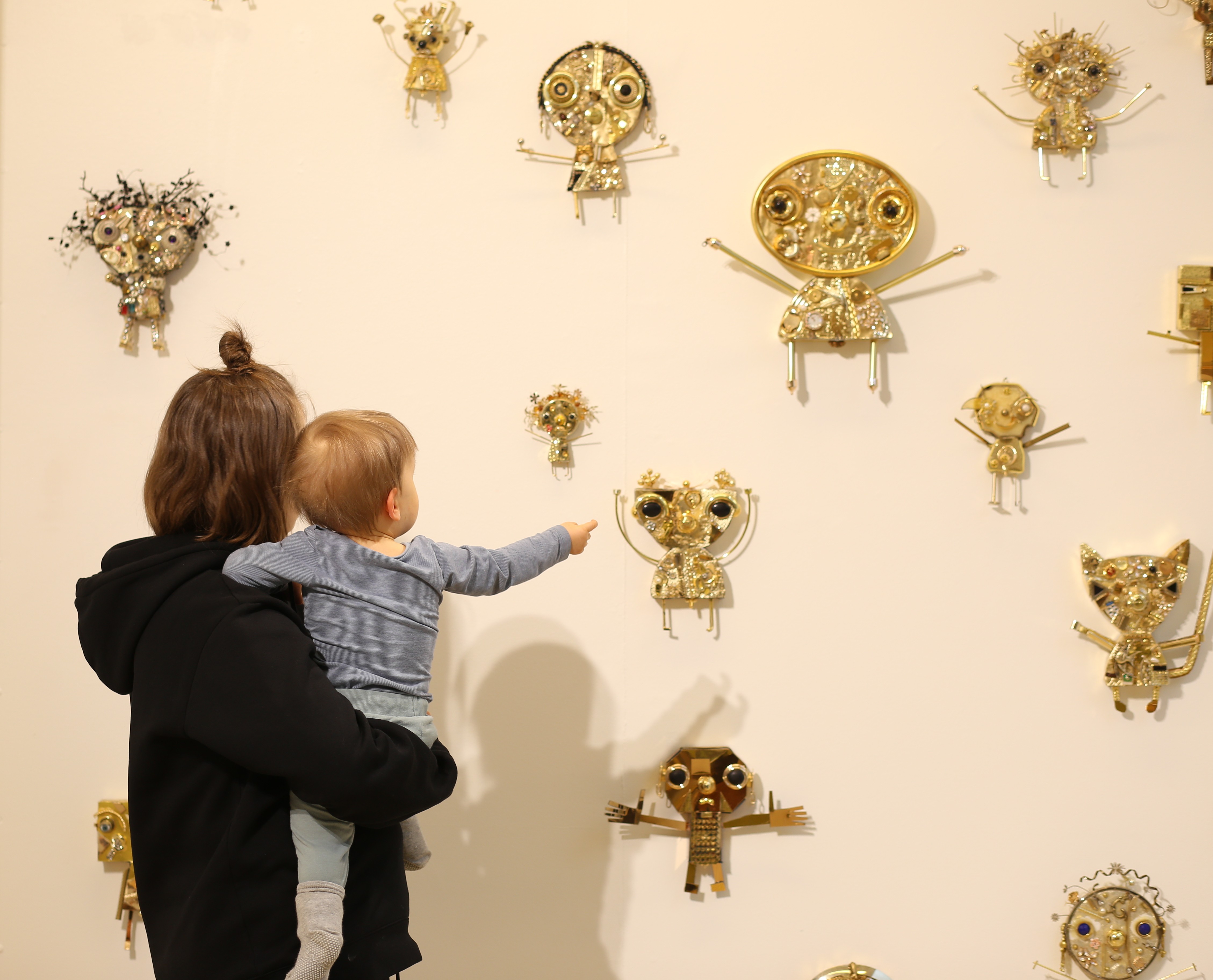 A baby and mother engaging with sculptures on a wall 