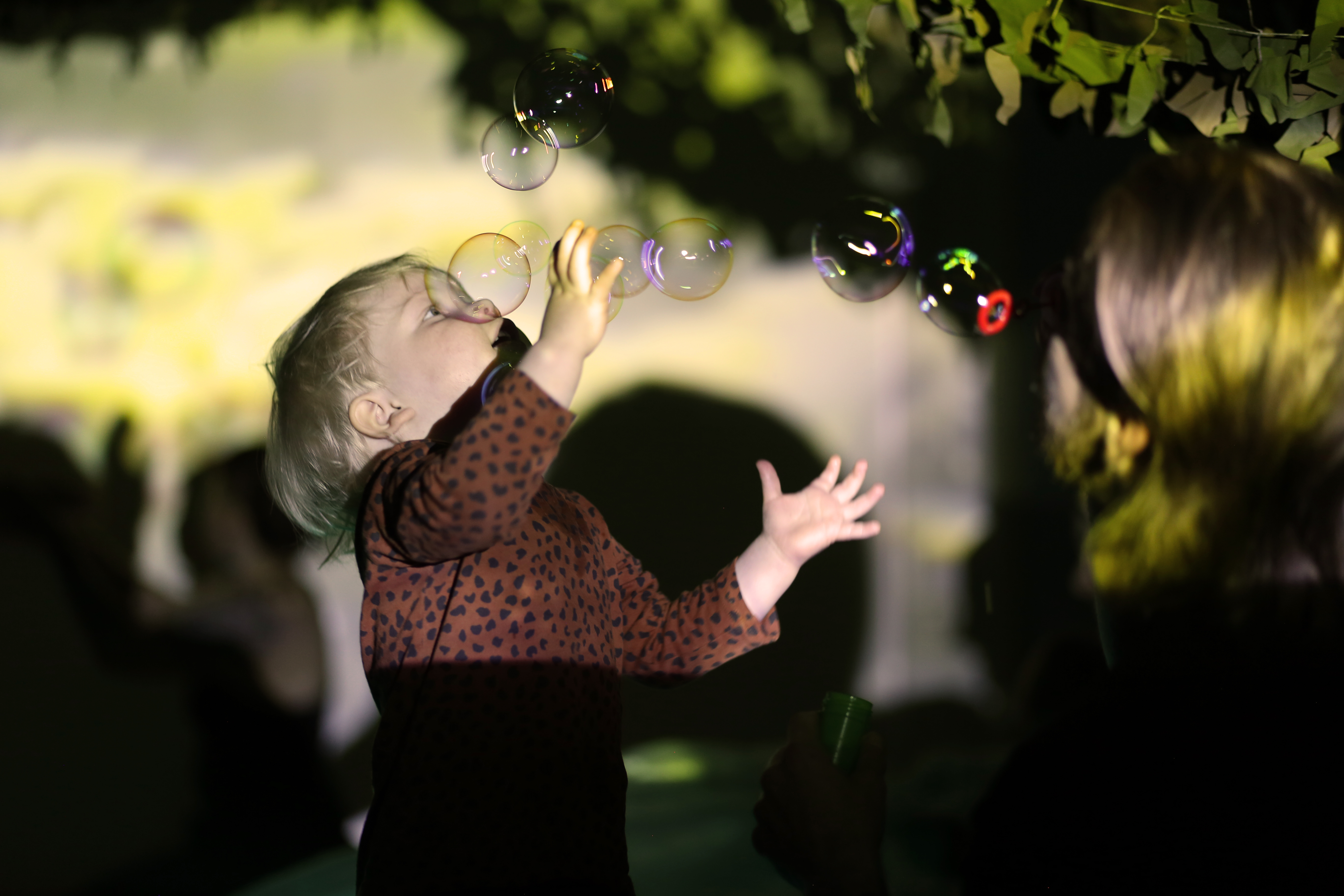 A baby in a darkly lit room with projections engaging with bubbles 