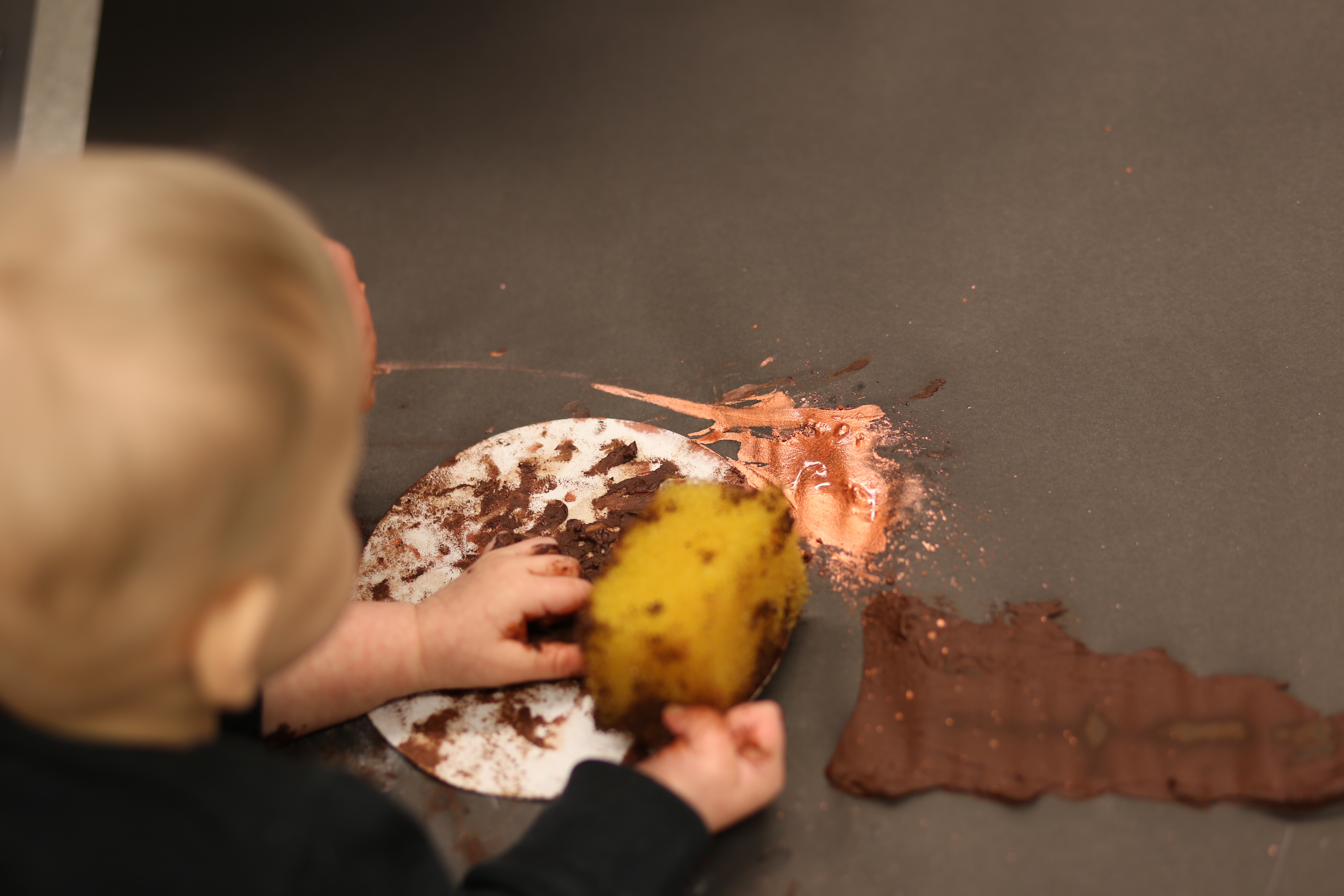 A baby's hands in brown material. They are holding a yellow piece of material 