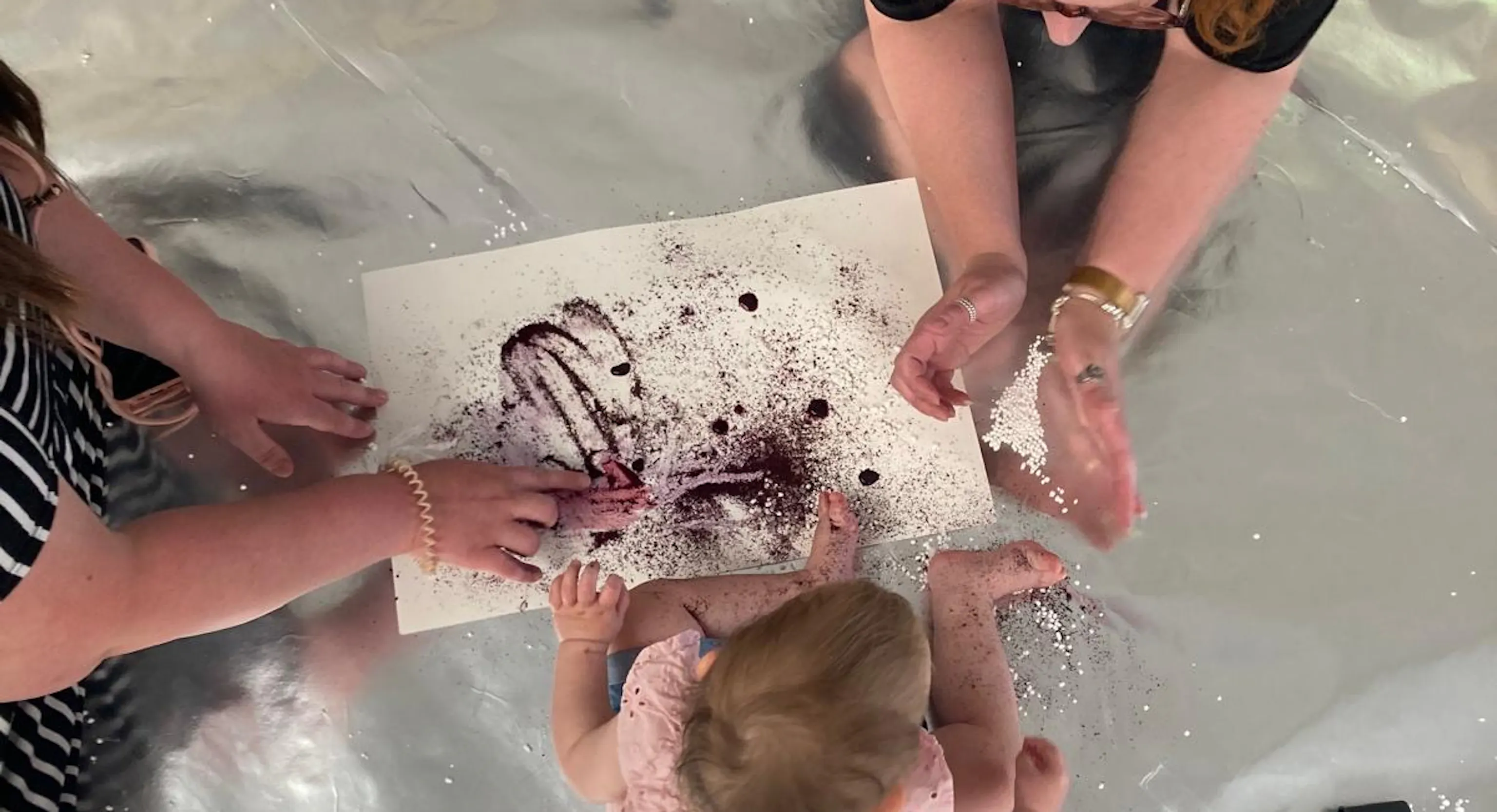 Two adult engage with a young child as they paint using blueberry juice and lemon.
