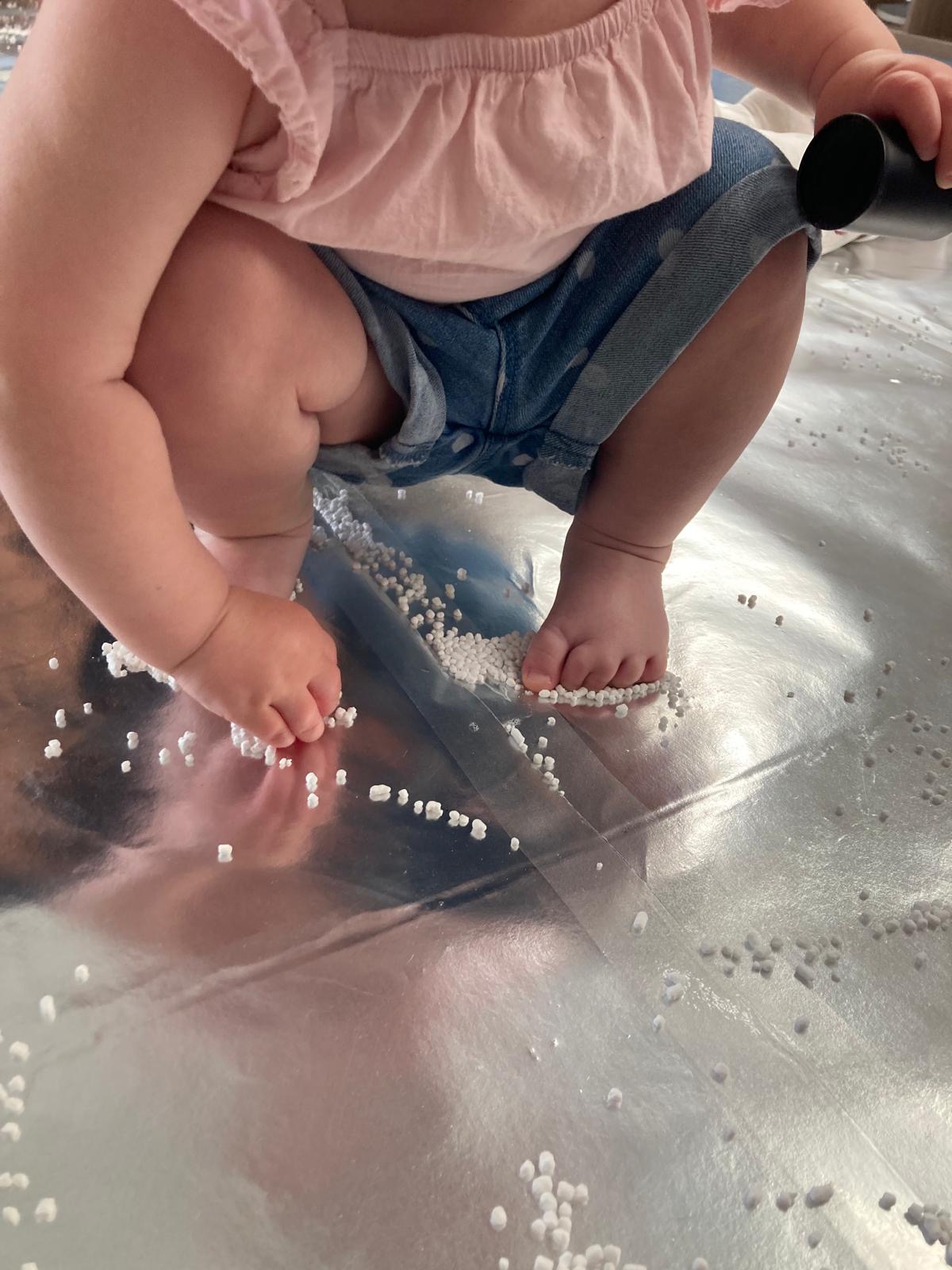 A young child interacts with the materials with both their hands and feet. They stand on a reflective, shiny floor.