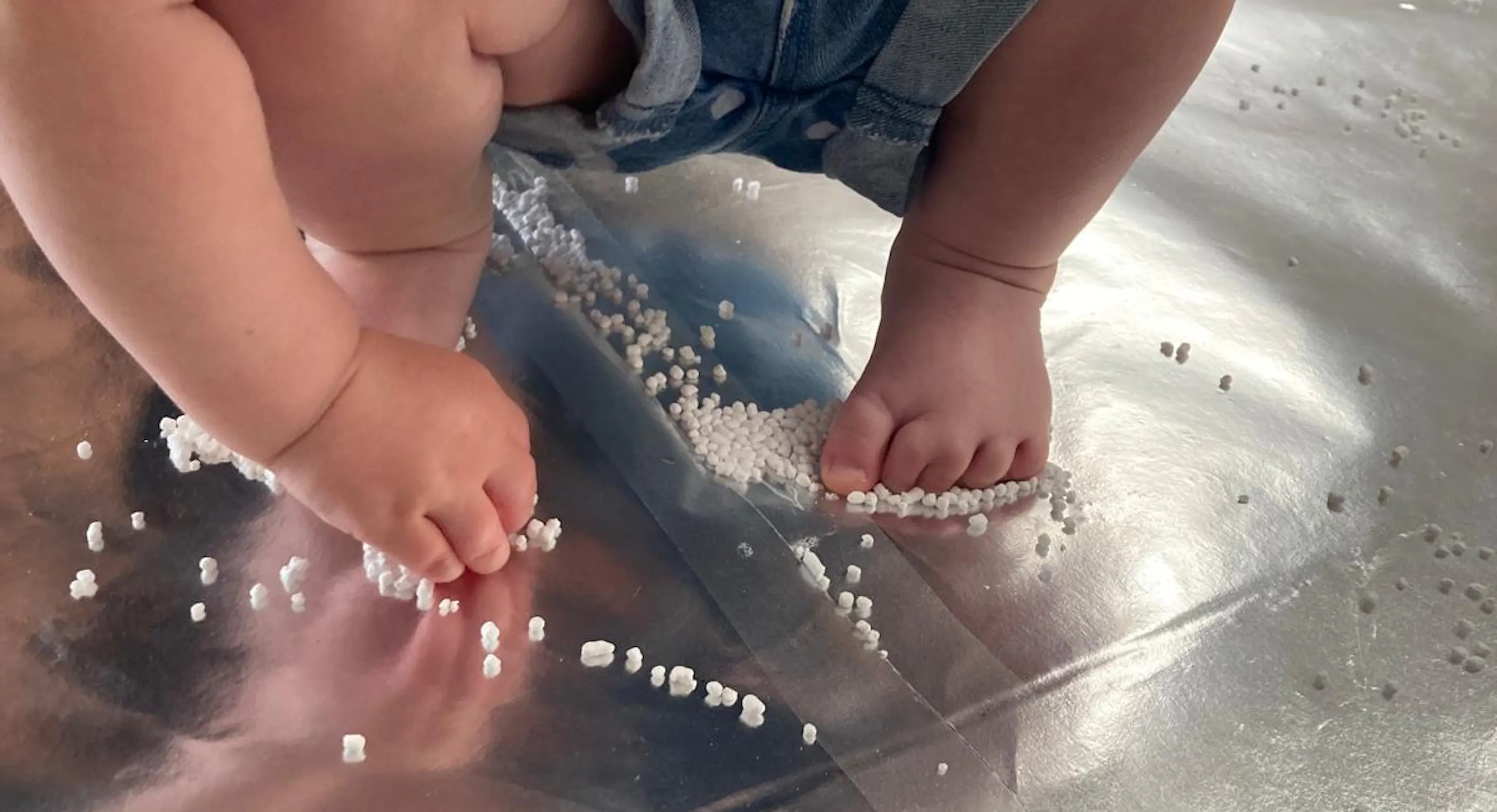 A young child interacts with the materials with both their hands and feet. They stand on a reflective, shiny floor.