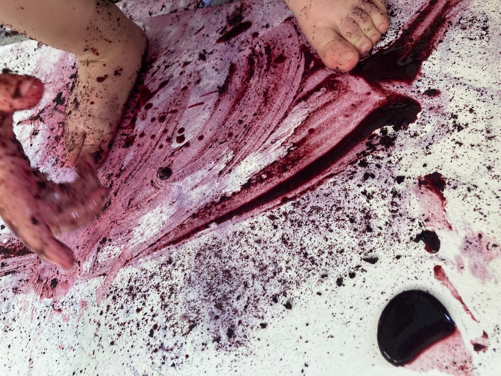 An abstract painting created by a young child's feet and hands. They have used blueberry juice and lemon to create the marks in the painting.