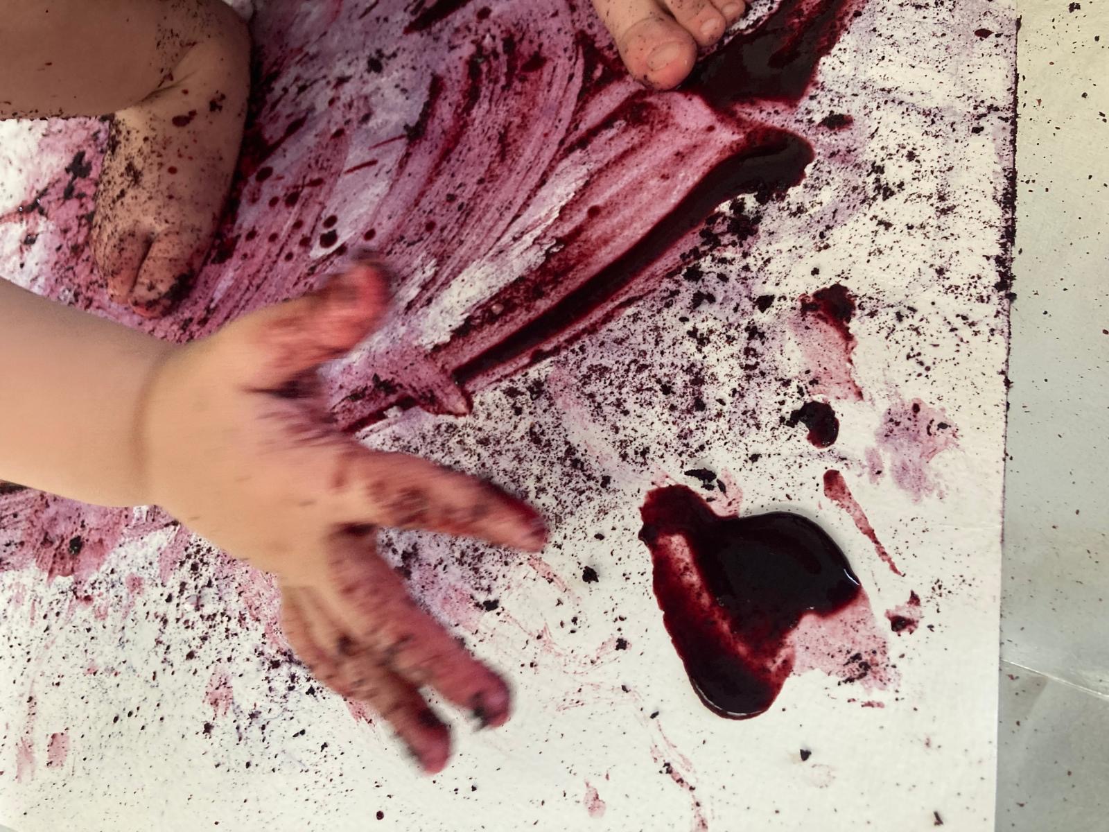 A picture of a young child's hand as they create an abstract painting with blueberry juice.