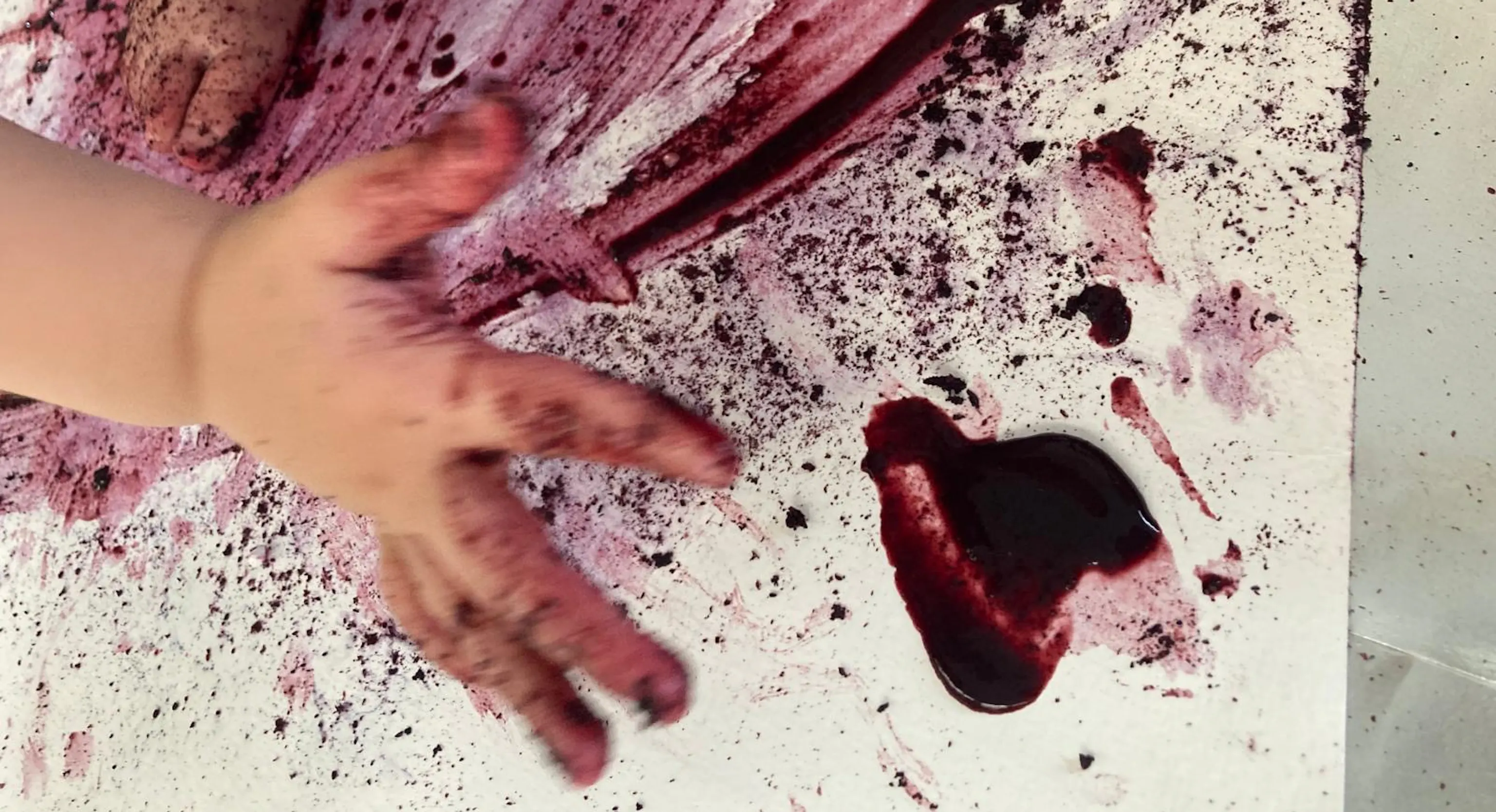 A picture of a young child's hand as they create an abstract painting with blueberry juice.