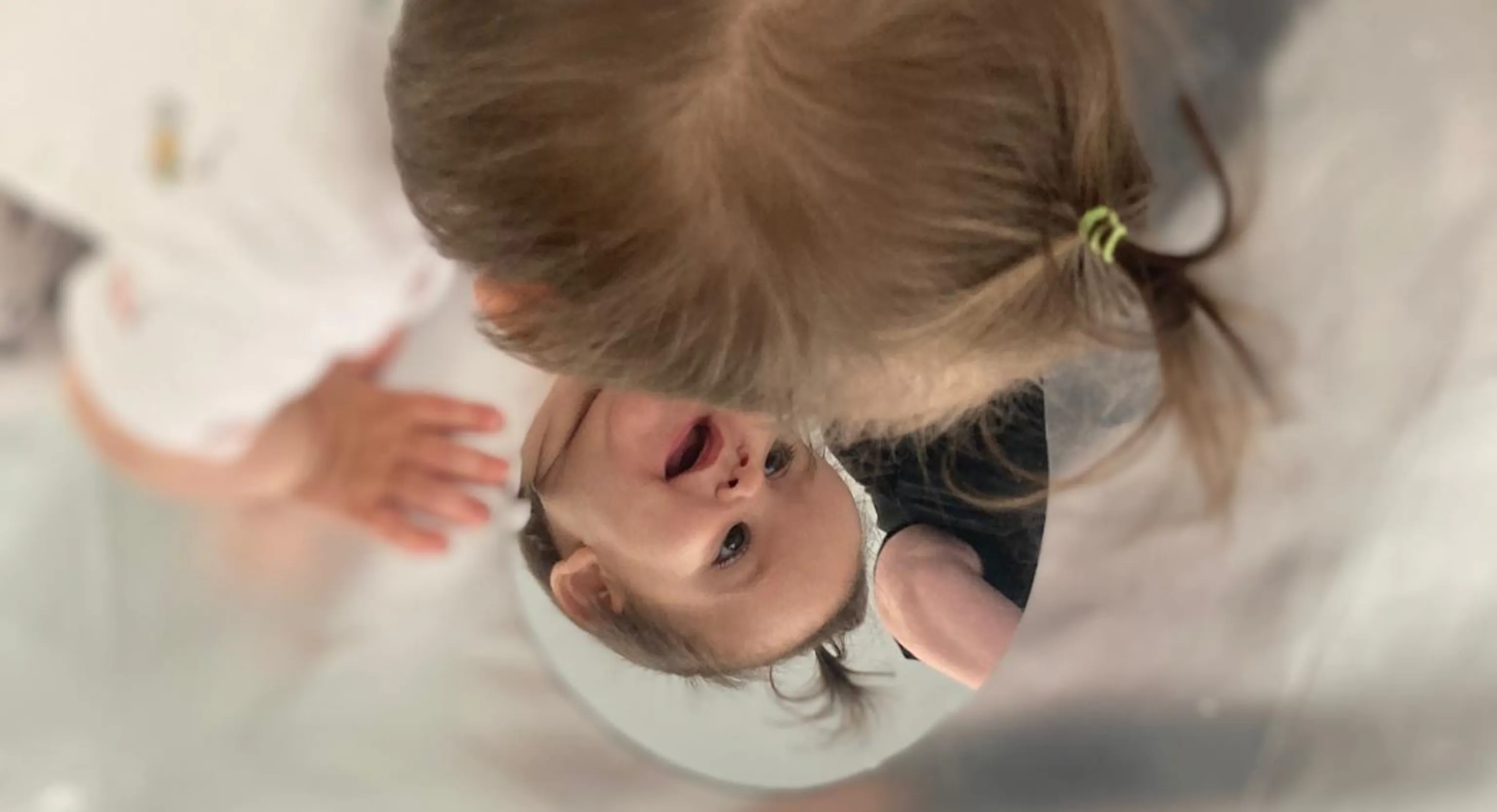 Young child looks at themselves in the mirror and smiles at their reflection.