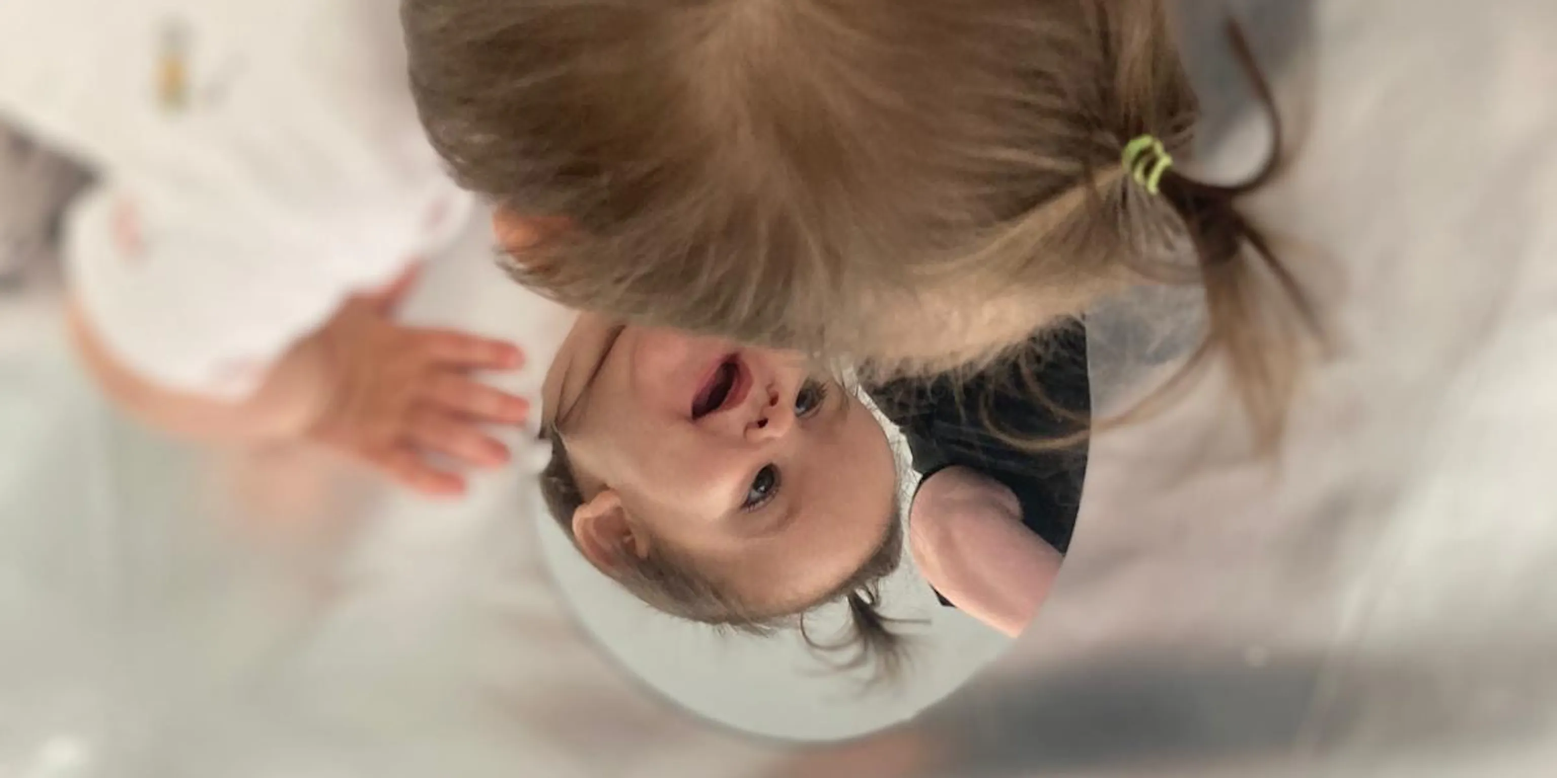 A young child engages with their reflection in a mirror. The mirror and child are on top of silver flooring which reflects the light in the room.