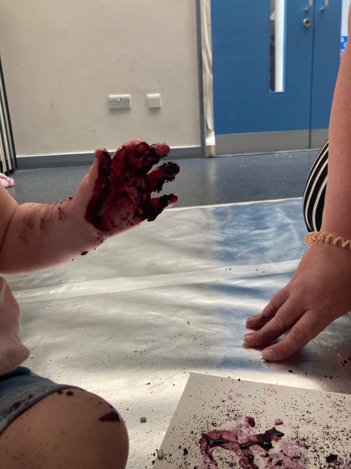 A close up of young child's hand covered in blueberry juice after they explore and engage with new materials.