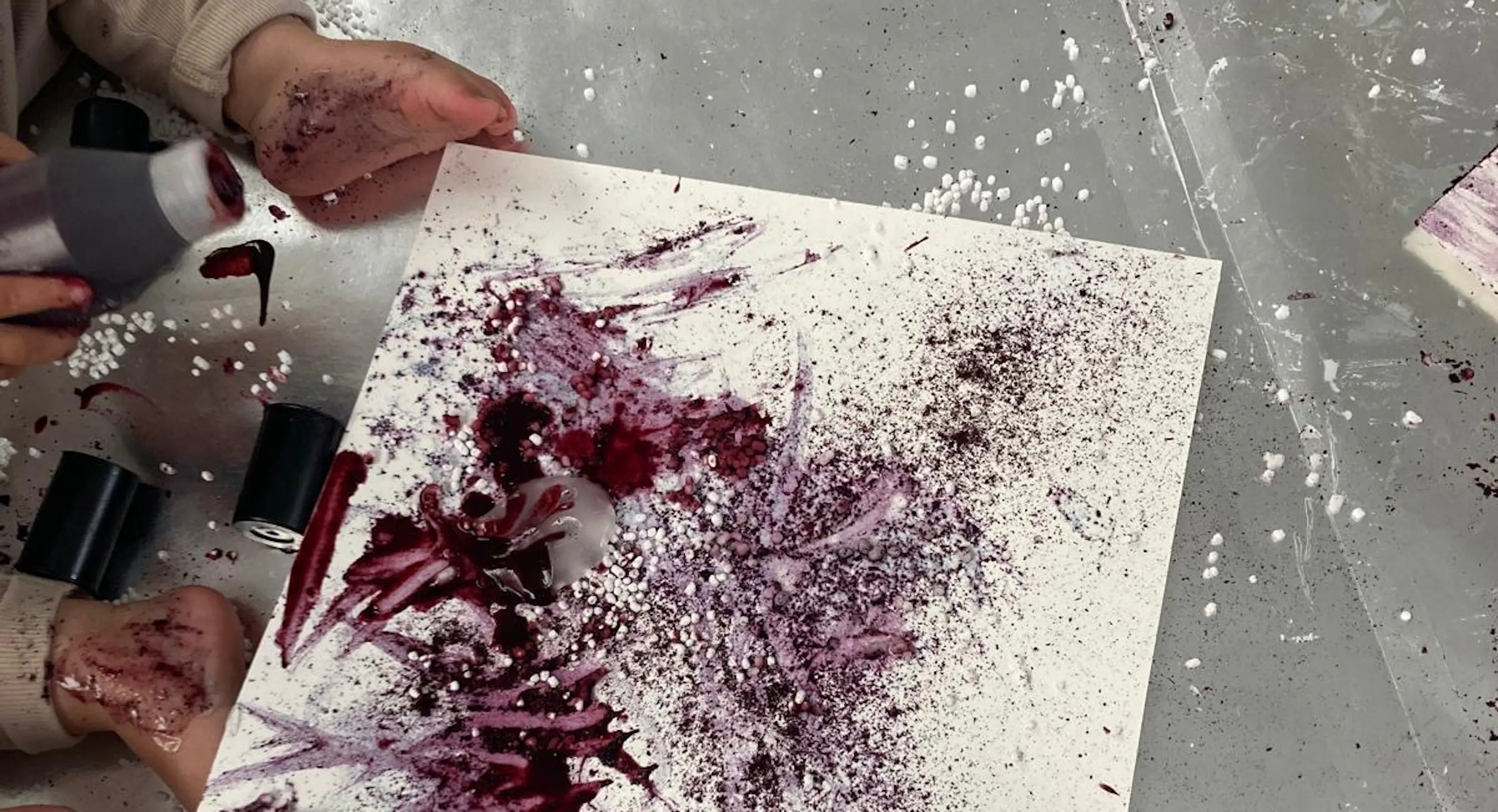 A young child paints an abstract image using blueberry juice and lemon.