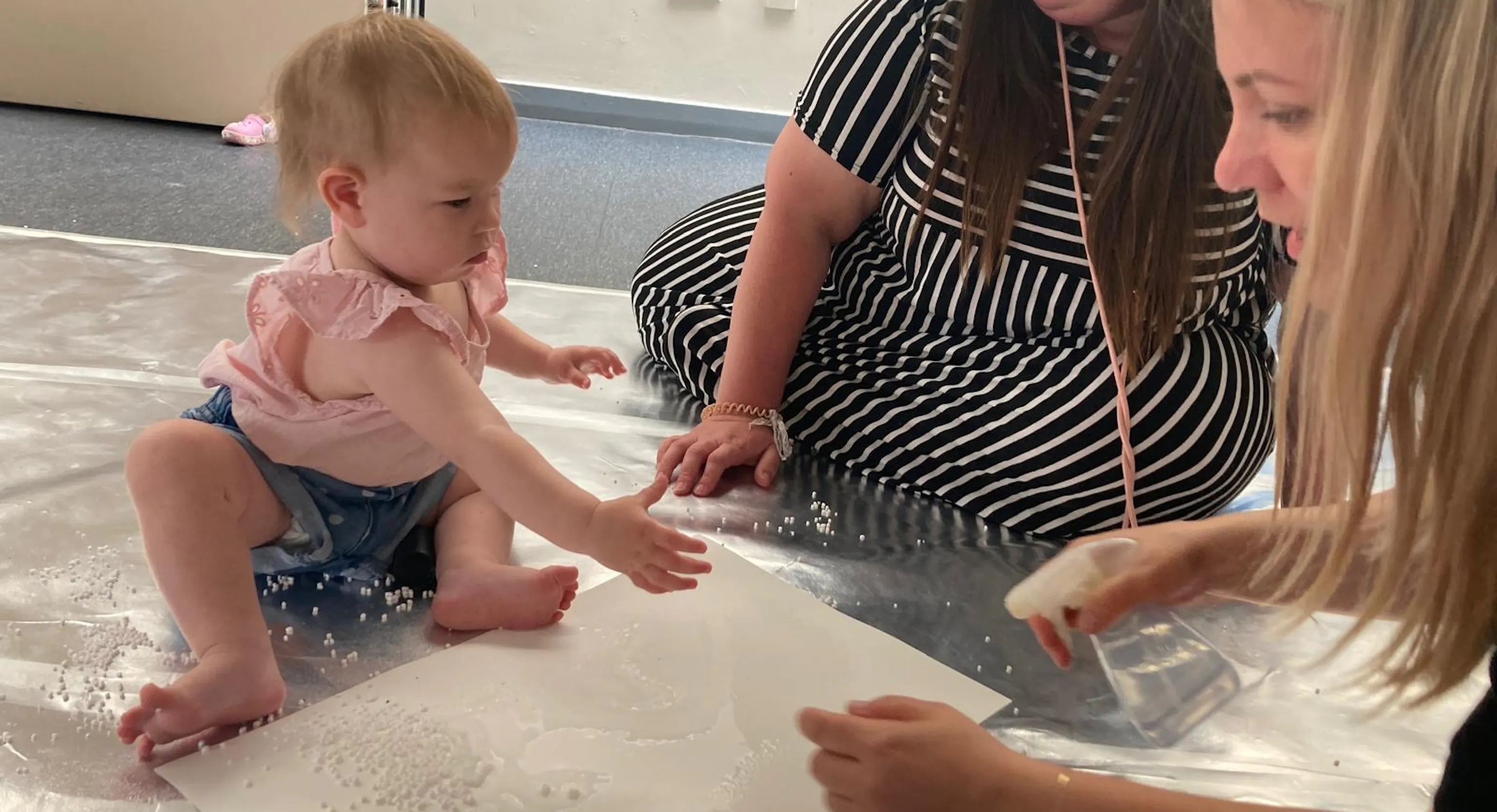 Two adult engage with a young child as they experiment with materials.
