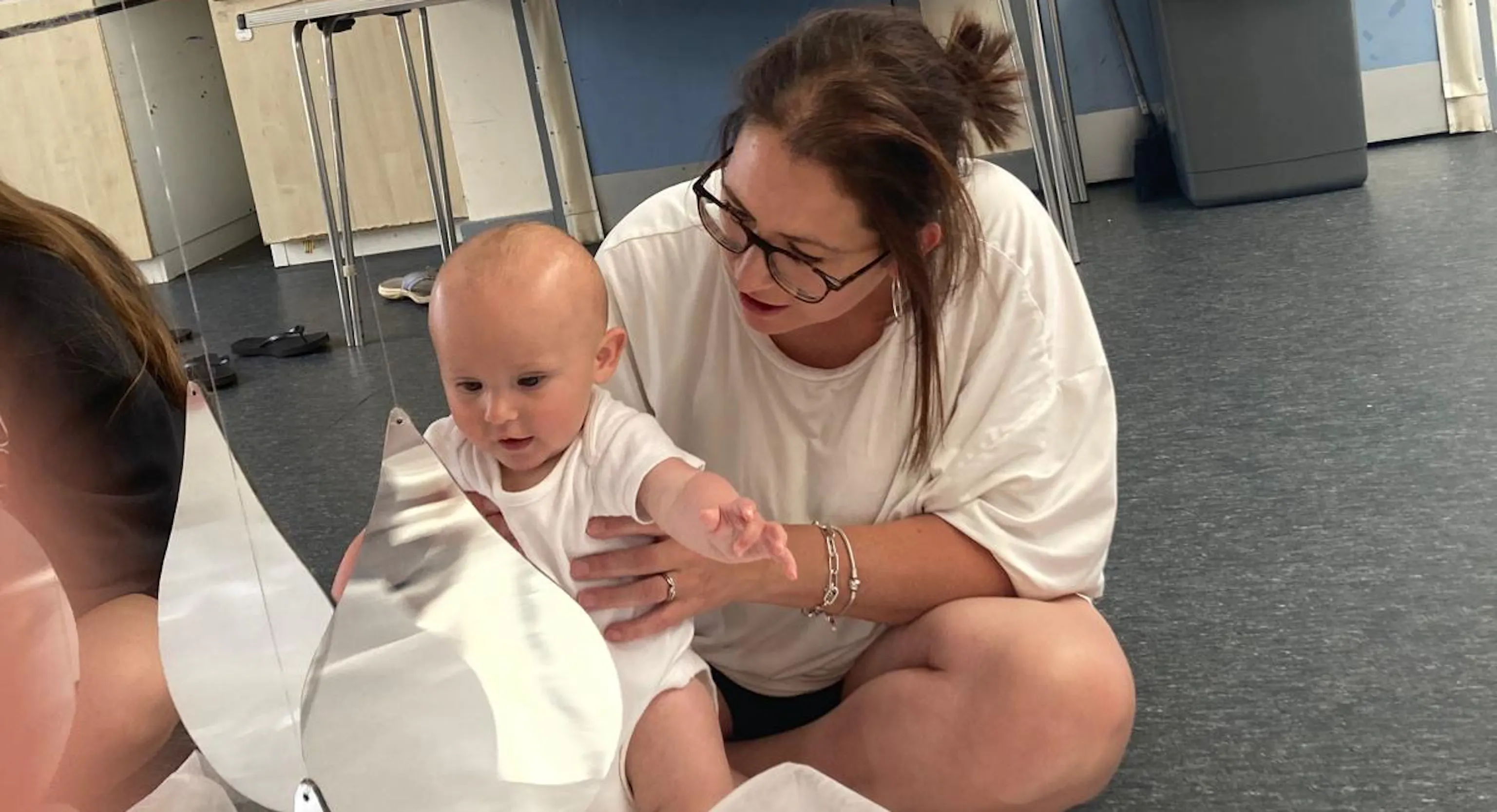 A young child and their carer look at their reflection in a teardrop mirror.