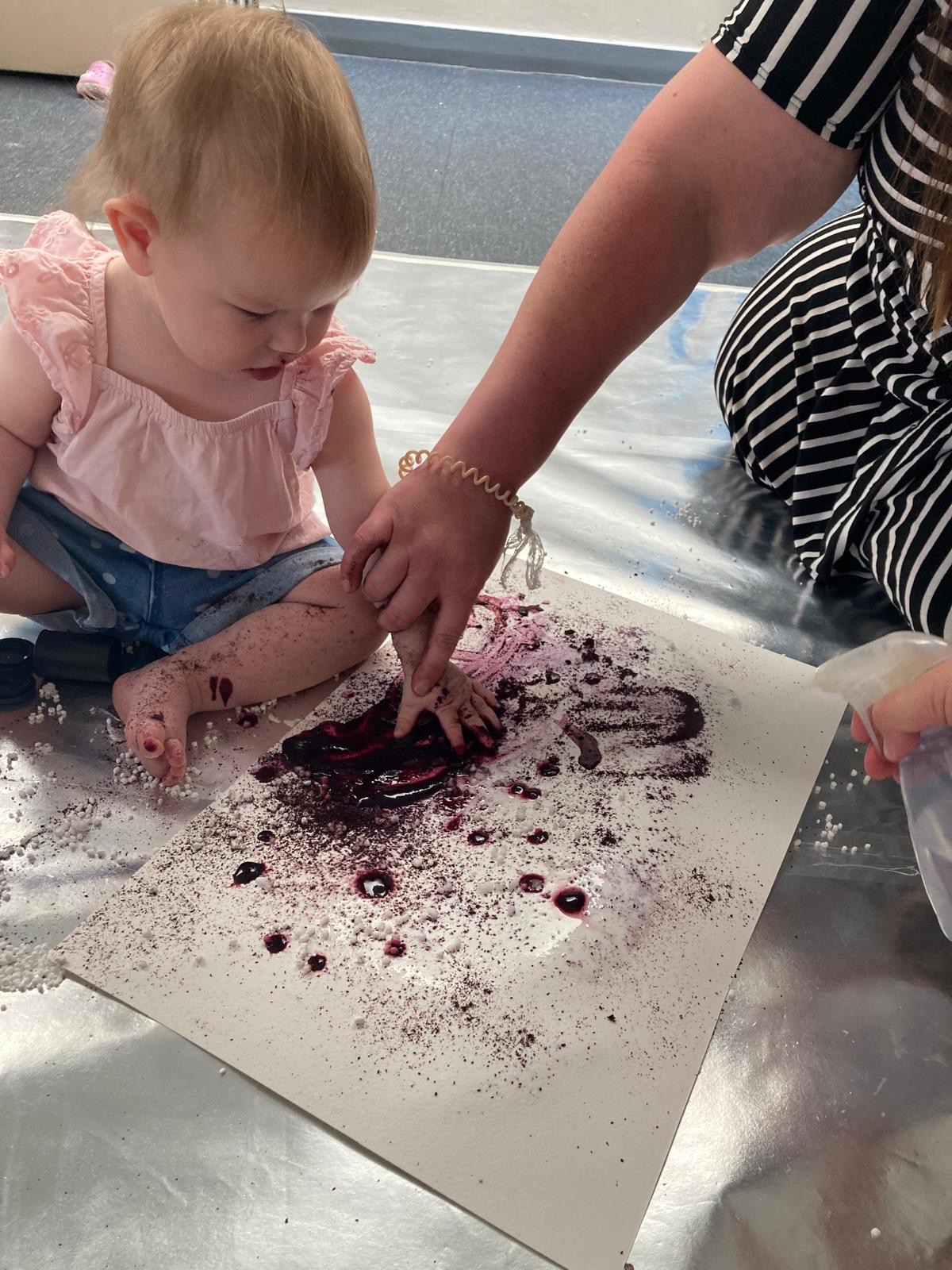 A young child enjoys getting messy and painting with blueberry juice and lemon.