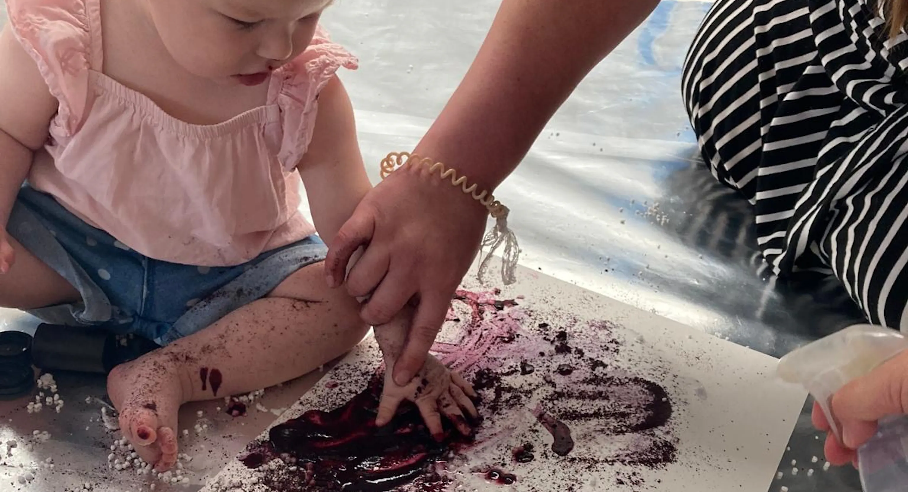 A young child enjoys getting messy and painting with blueberry juice and lemon.
