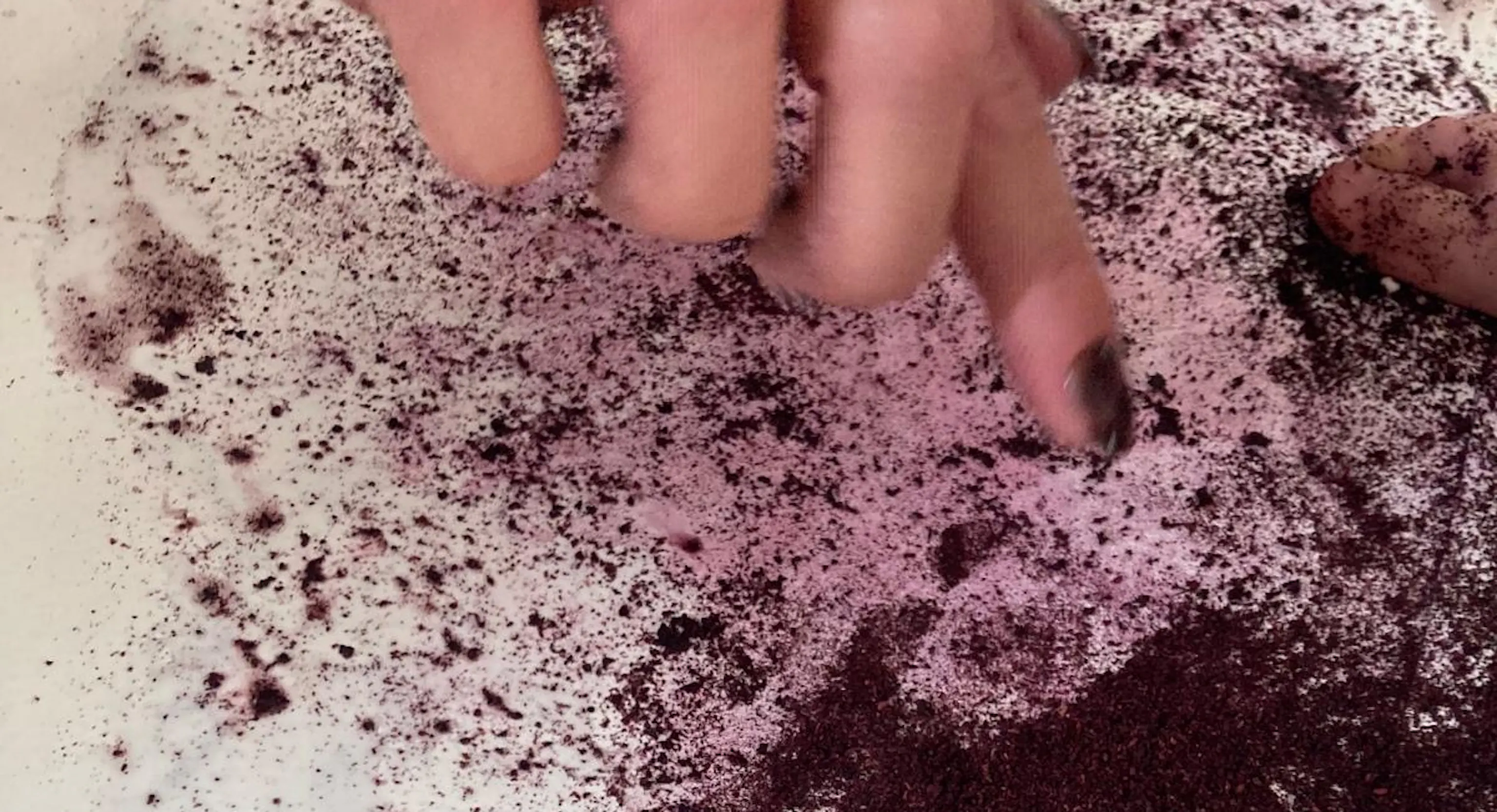A close up of an adult hand pointing to the marks made with blueberry juice and lemon juice on a piece of paper.