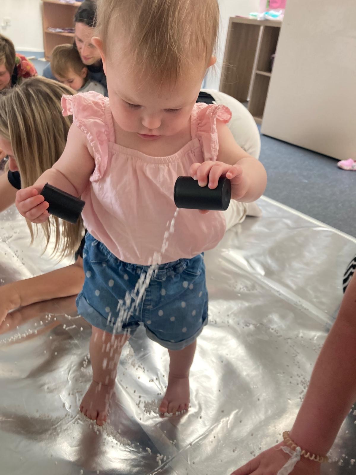 A young child explores pouring water from a vessel onto other materials.