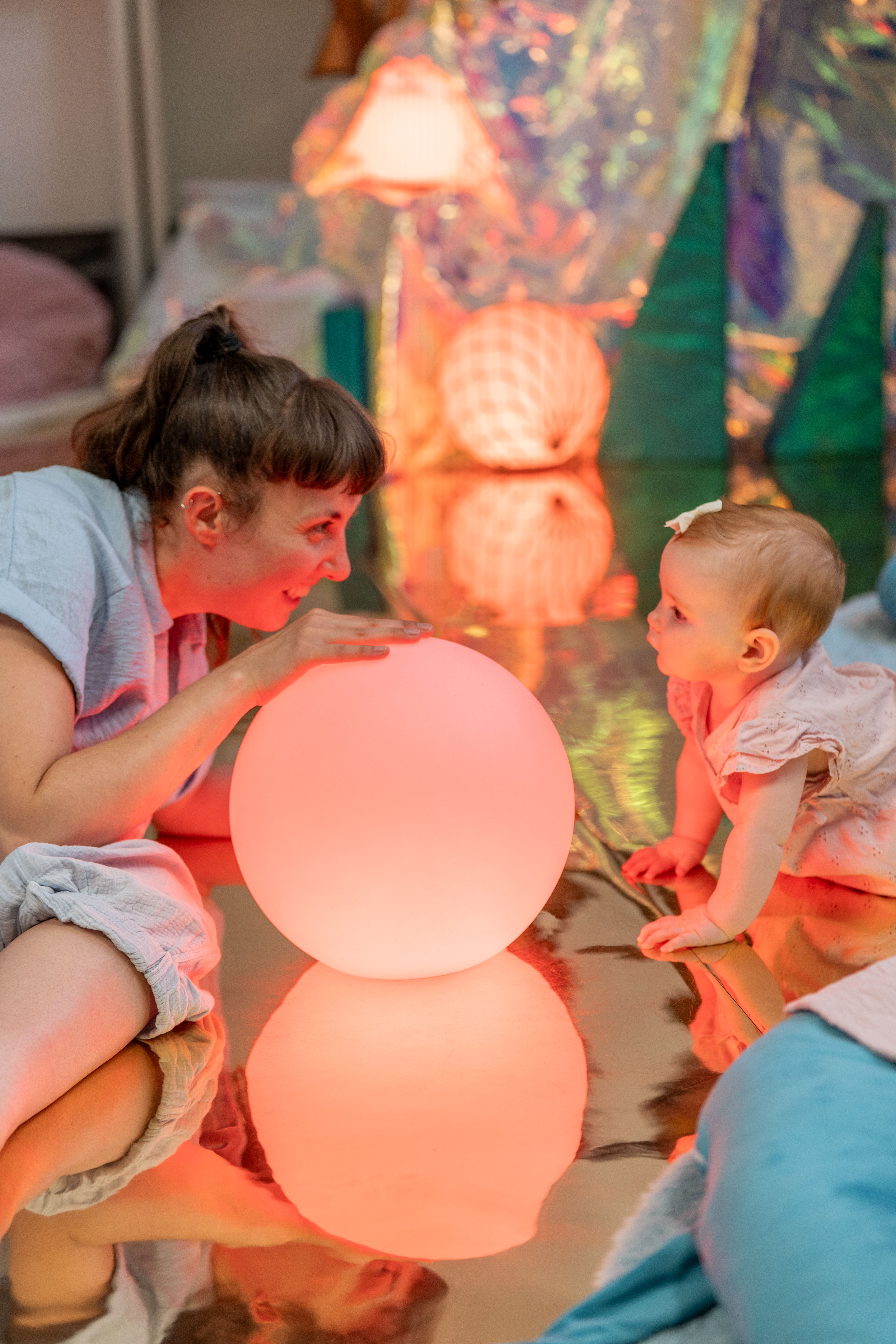 An artist and baby lying on the floor and looking at each other. There are colourful balls around and inbetween them 