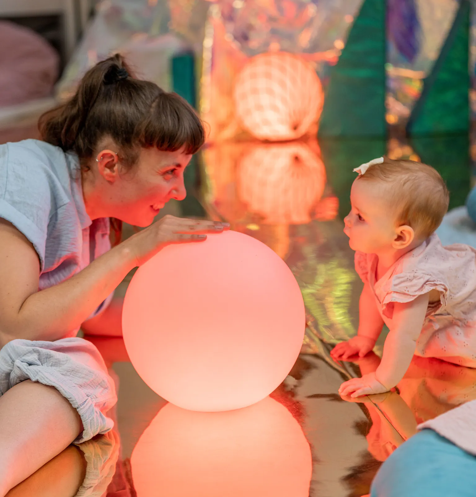 An artist and baby lying on the floor and looking at each other. There are colourful balls around and inbetween them