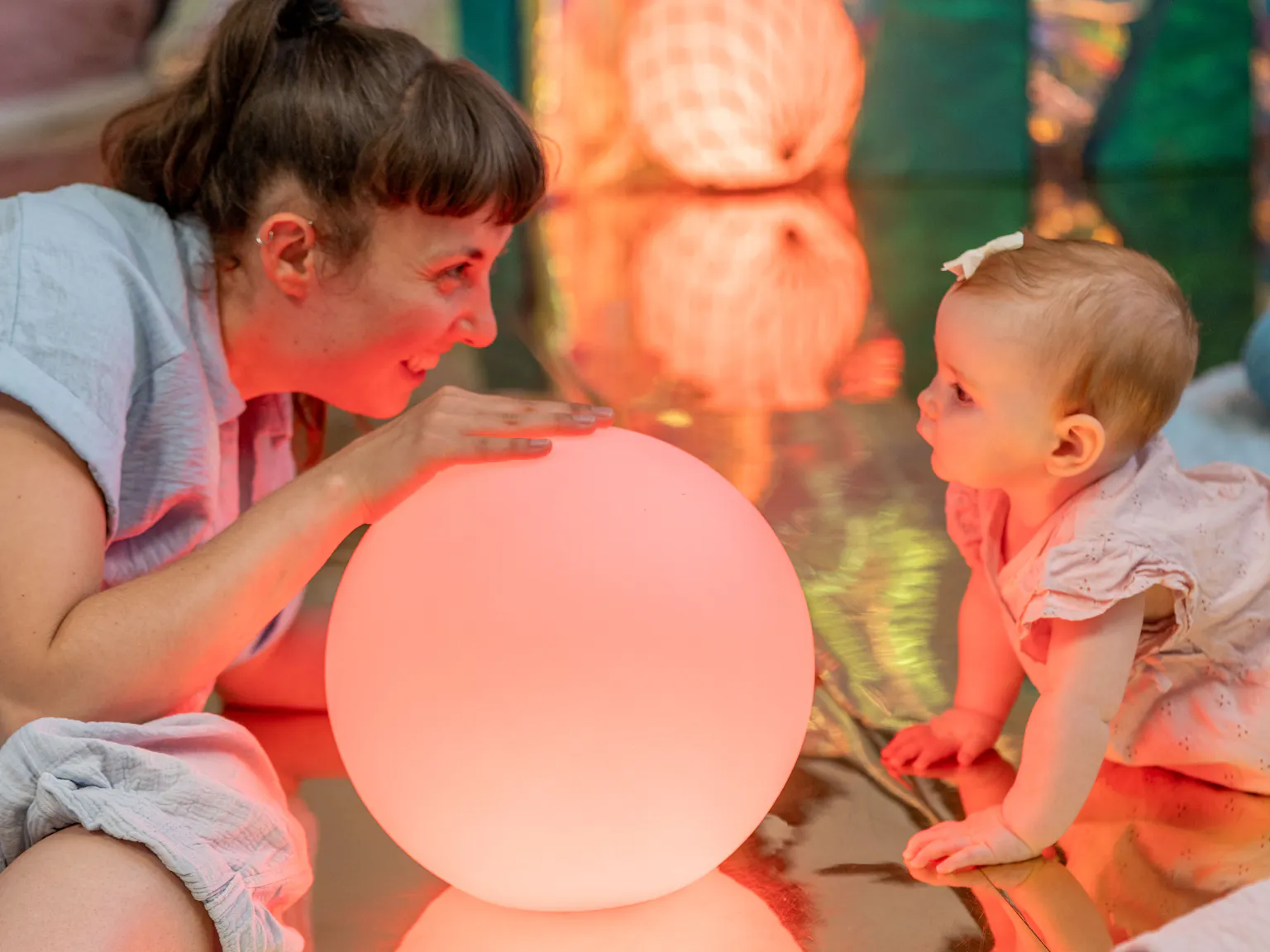 An artist and baby lying on the floor and looking at each other. There are colourful balls around and inbetween them