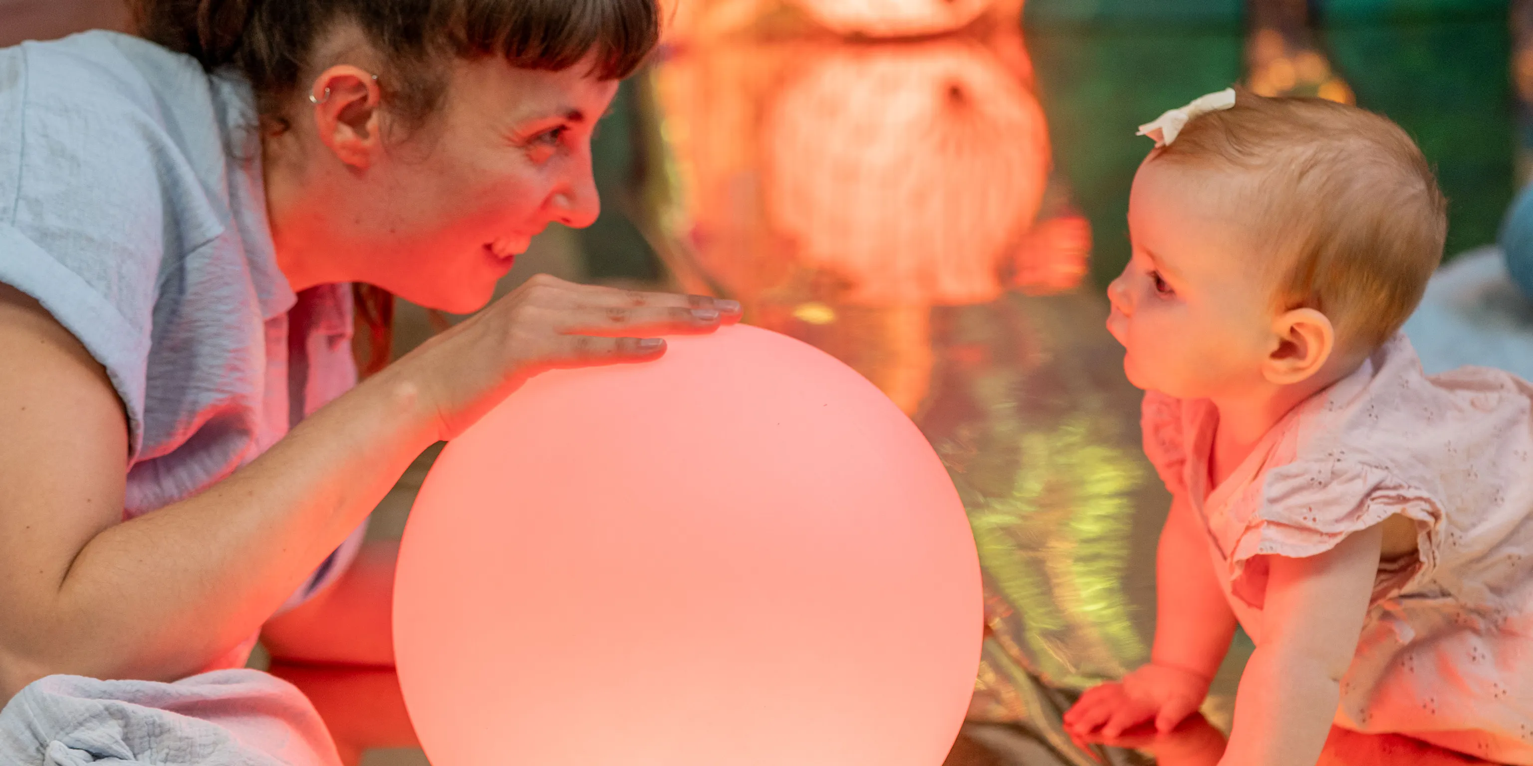 An artist and baby lying on the floor and looking at each other. There are colourful balls around and inbetween them