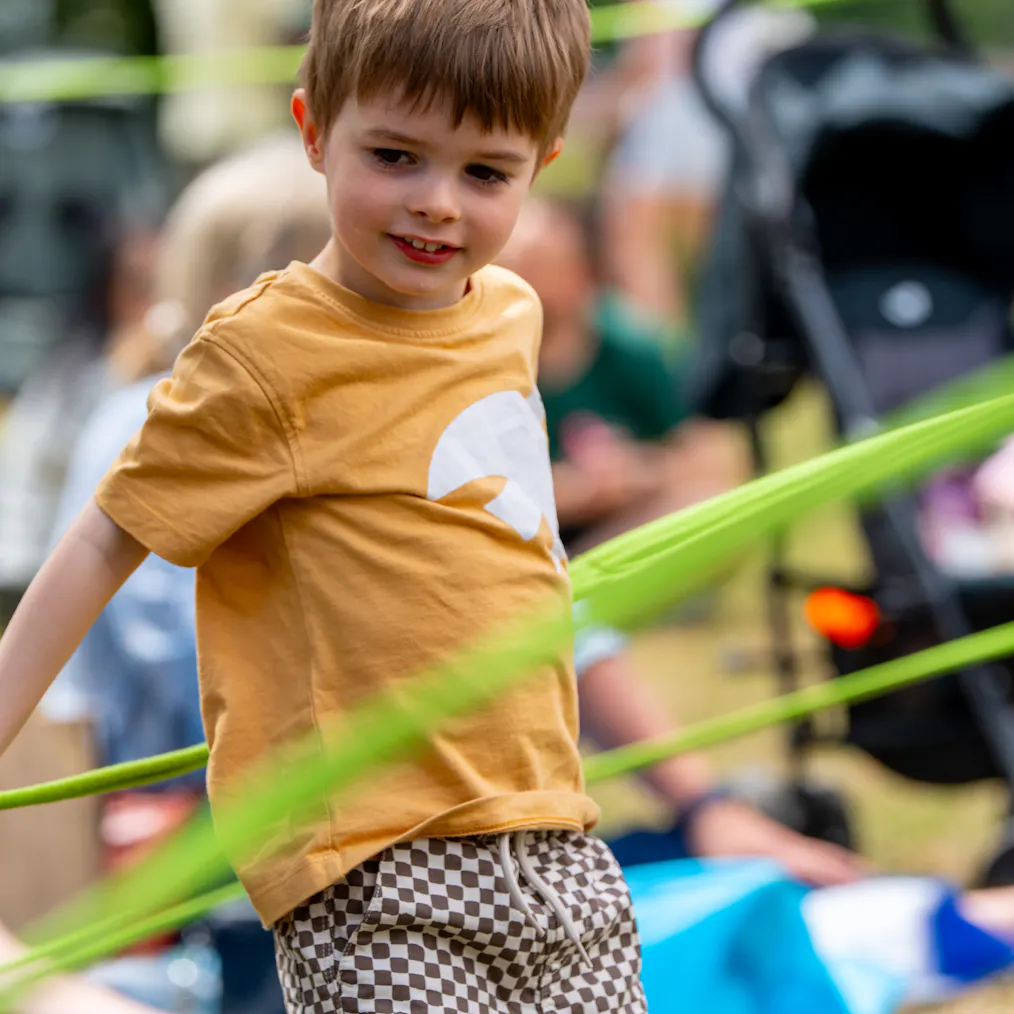A child smiling with green rope around them as part of a performance