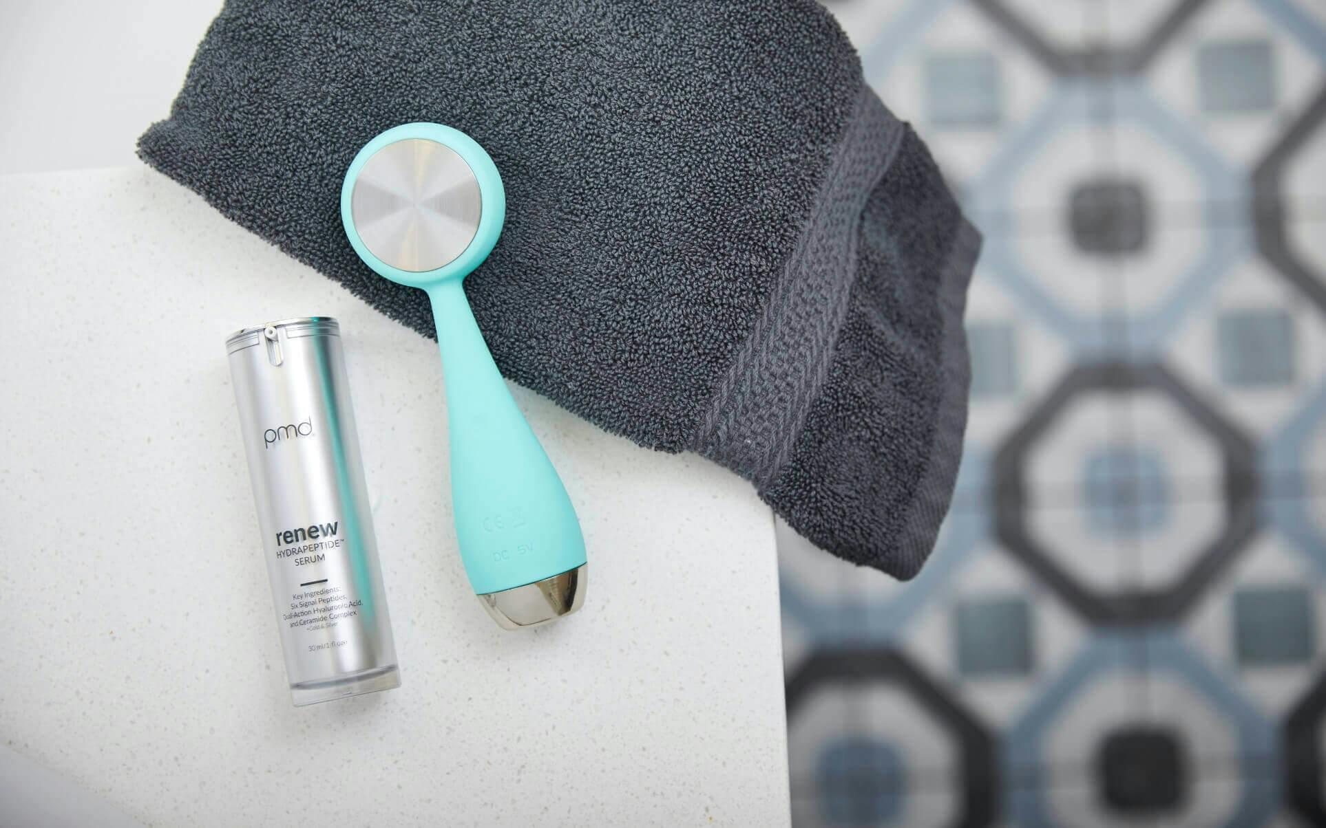 Teal PMD Clean Pro with renew HydratingPeptides™ Serum on bathroom countertop with grey towel. 