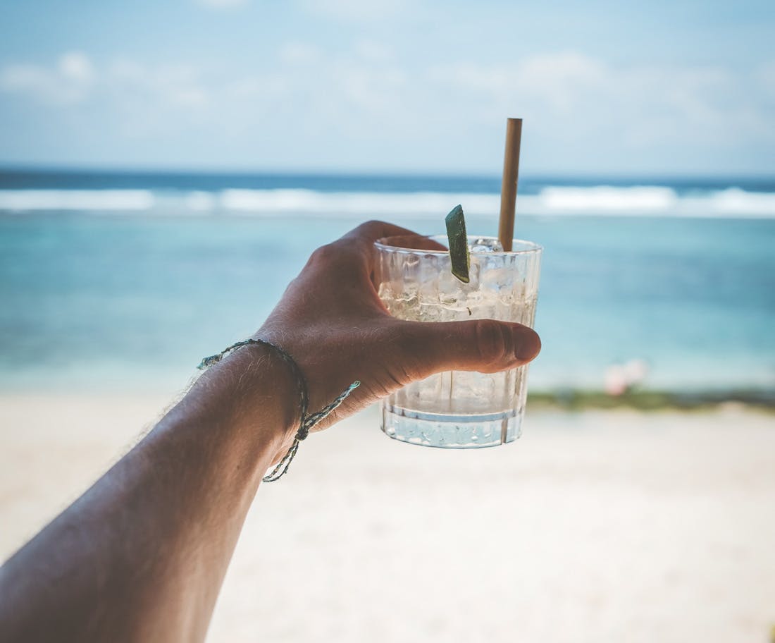 Image of a arm reaching out holding a cocktail looking out to the beach