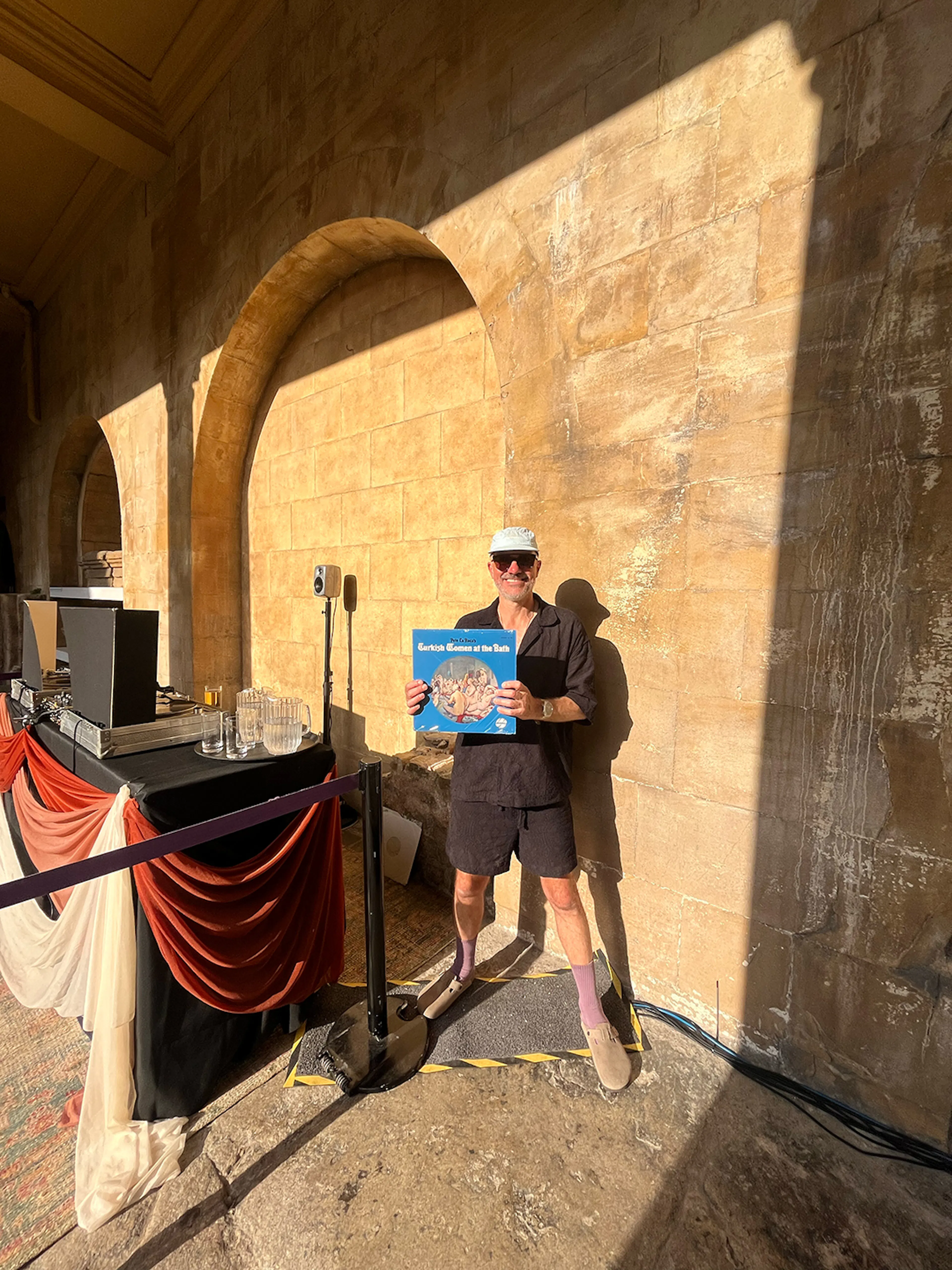 Tim Spencer holding a vinyl record next to the dj riser inside the Great Baths at The Roman Baths. 