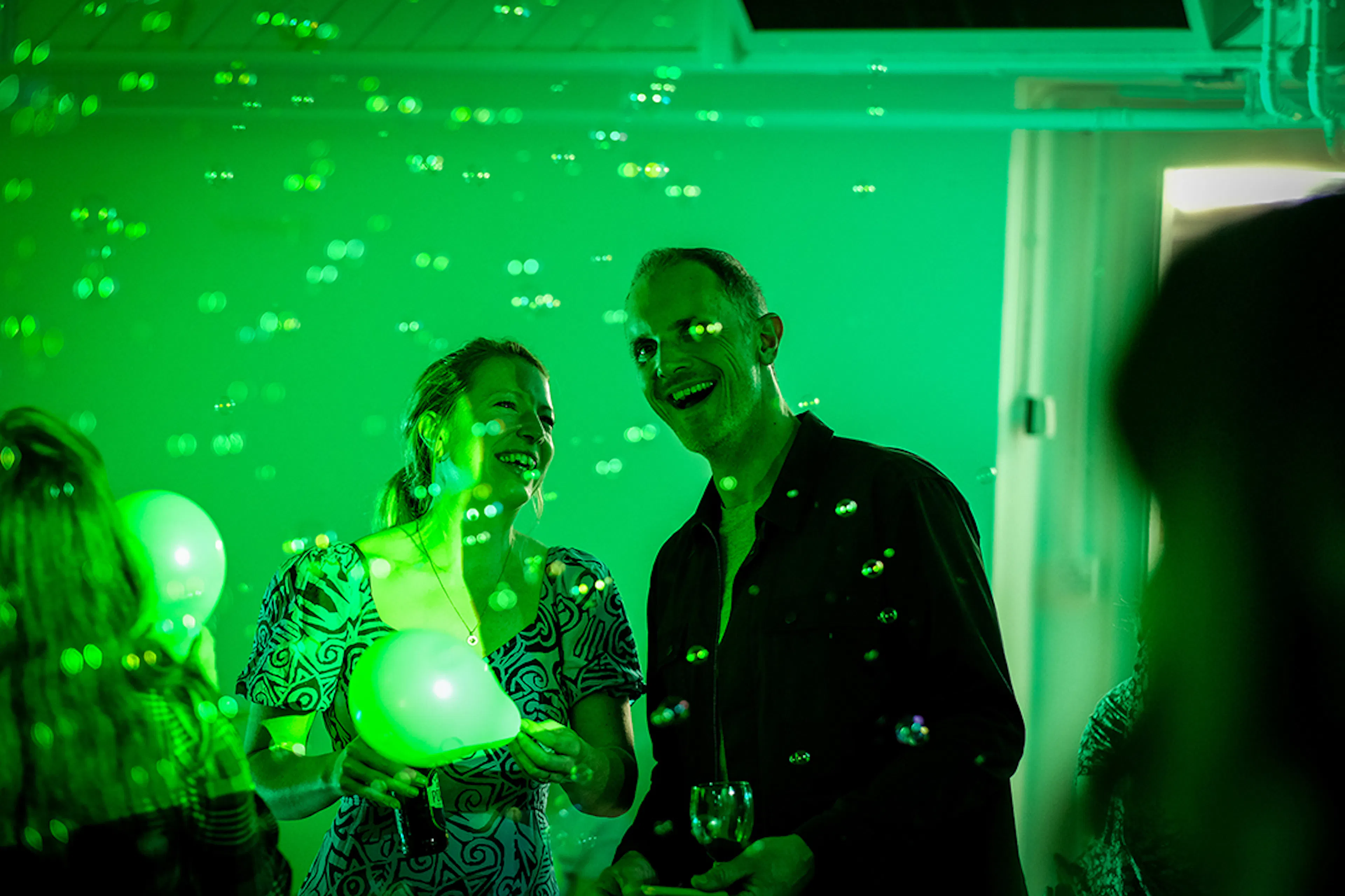 Audience members holding a balloon smiling at the bubbles floating around them. 