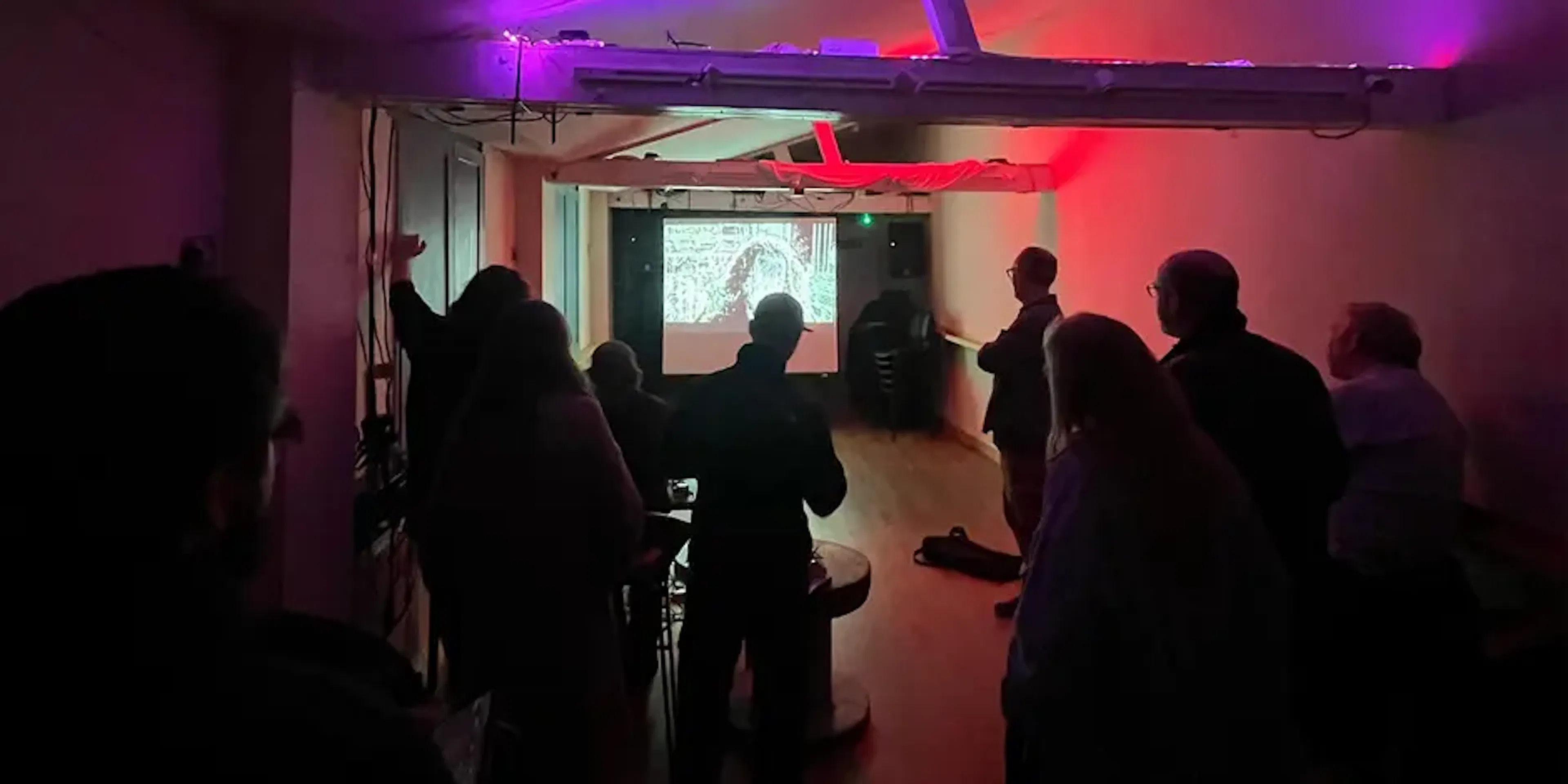 A wide shot of audience members at the audio visual meet up looking at a projection.