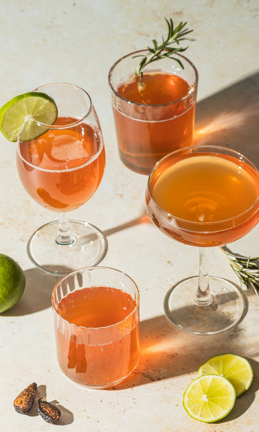 Four copper-colored beverages in assorted glassware, surrounded by garnishes.
