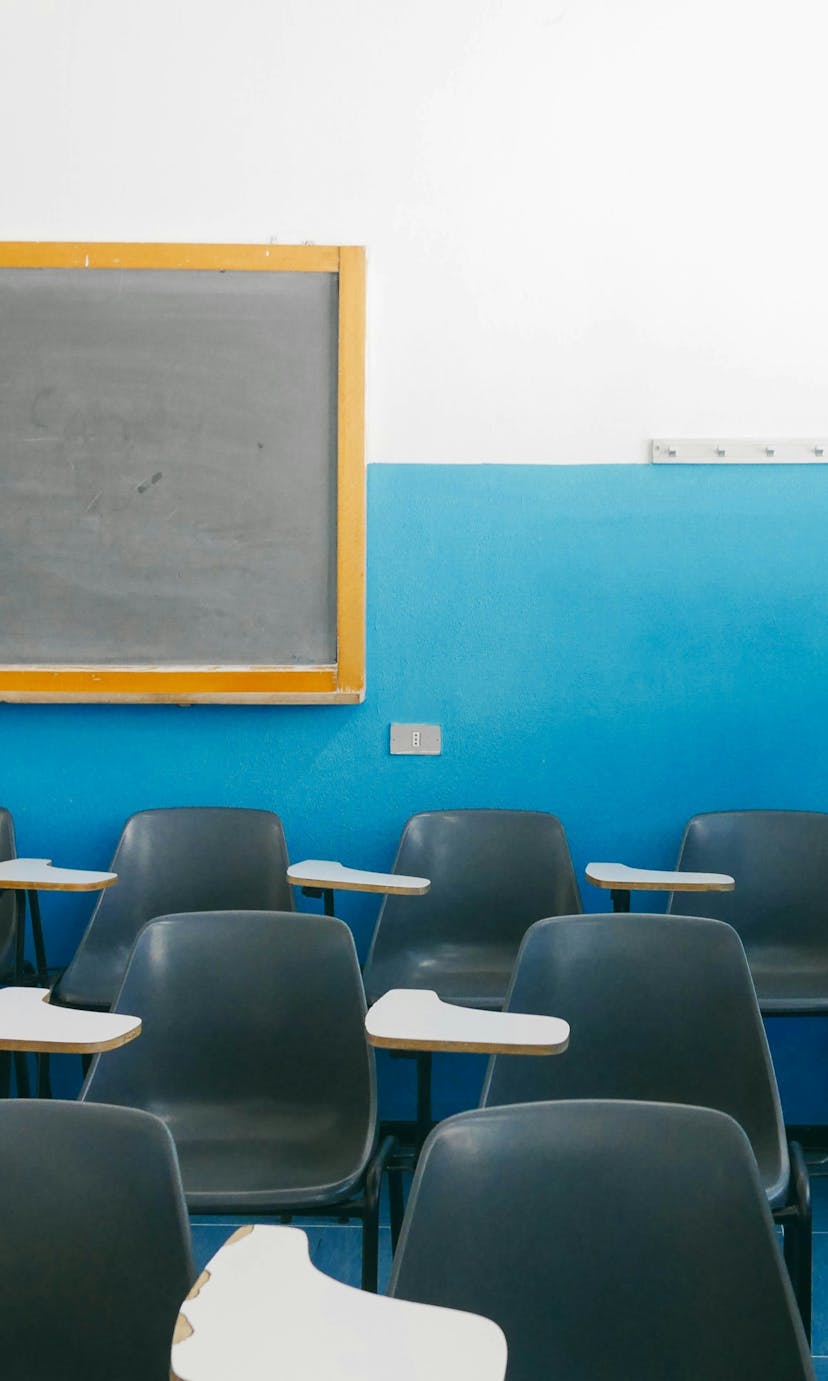 Empty desks in a classroom with blue walls and a yellow-trimmed chalkboard