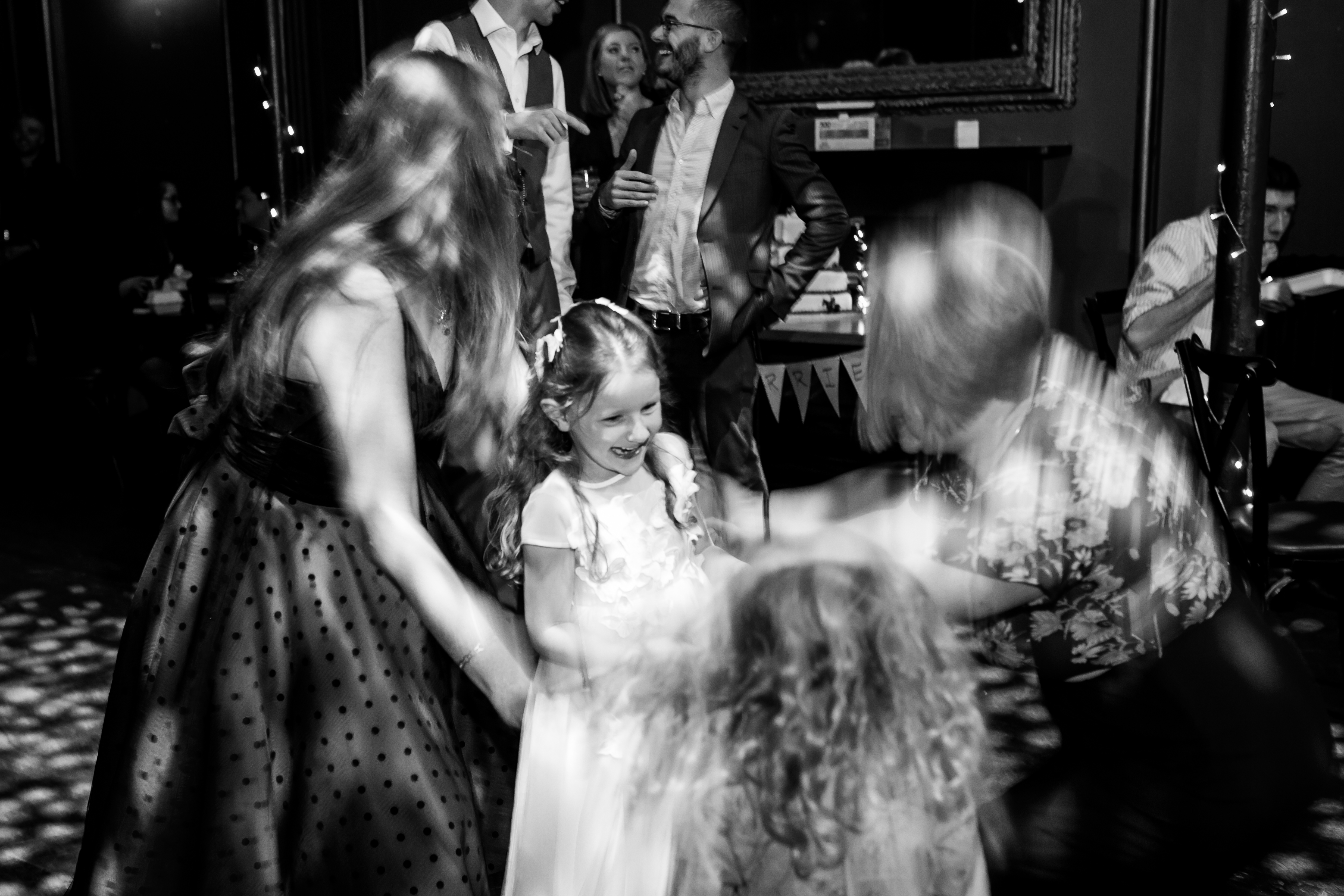 Poppy Walker Children's Celebrant. Black and white. A young girl excitedly smiles, with blurry women surrounding her. 