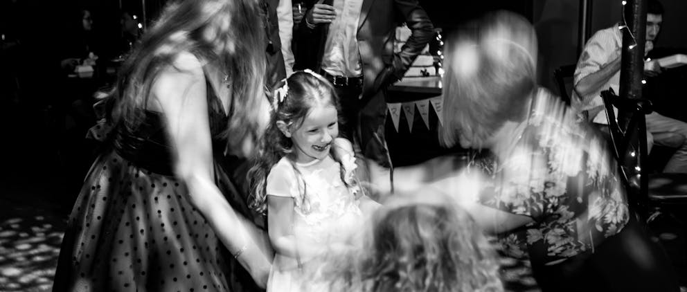 Poppy Walker Children's Celebrant. Black and white. A young girl excitedly smiles, with blurry women surrounding her. 