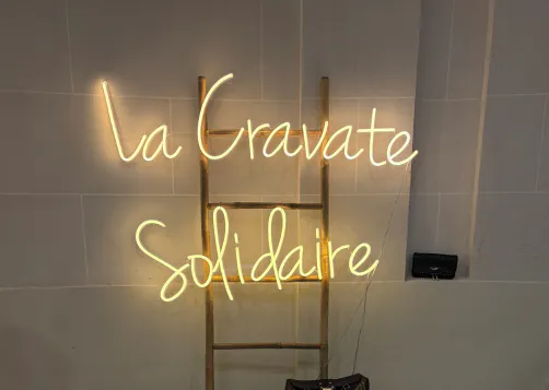 un panneau lumineux où il y est écrit la cravate solidaire et derrière il y a une échelle