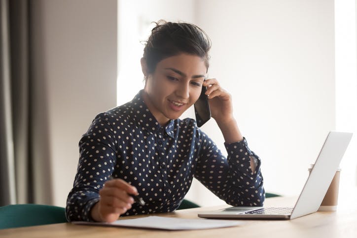 Mulher na mesa falando ao telefone a anotando informações em um papel