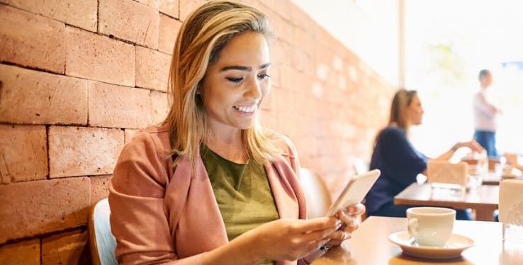 mulher sorridente sentada em uma mesa com o celular nas mãos