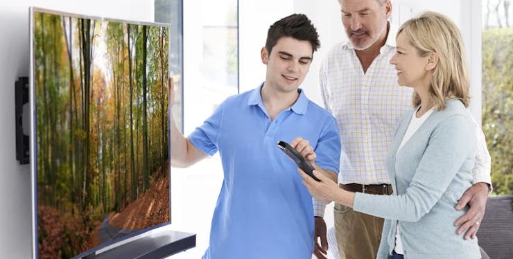 Pessoa ajudando a instalar uma TV para um casal