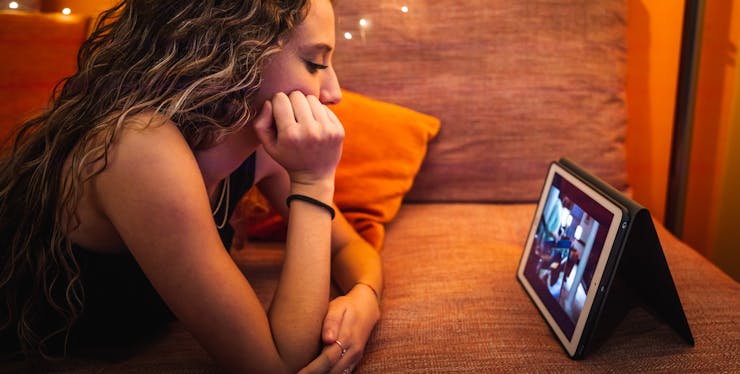 menina deitada no sofá assistindo série em um tablet