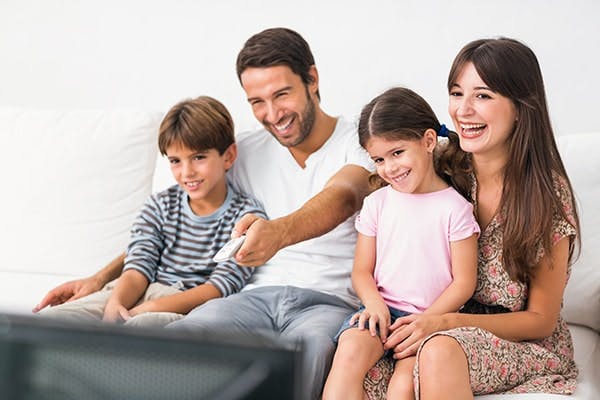 Vantagens SKY: família feliz assiste TV e pai aperta controle remoto