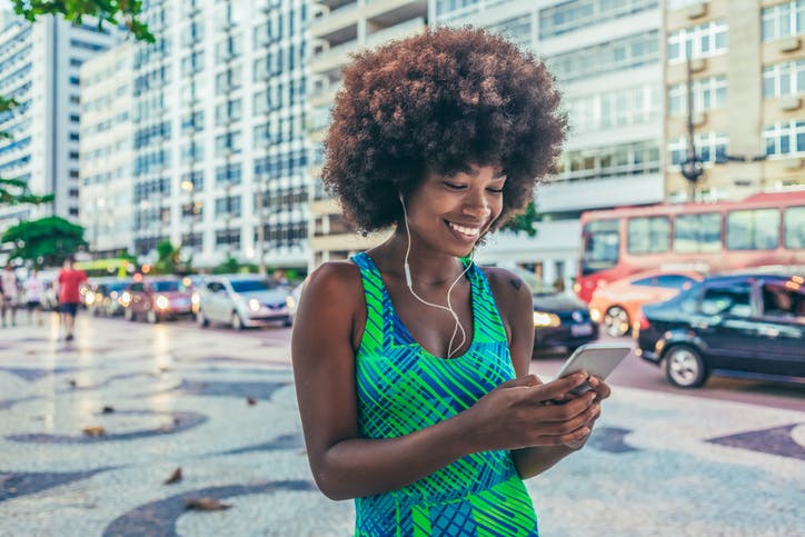 Mulher caminhando na rua e escutando música no celular com seu plano da Claro